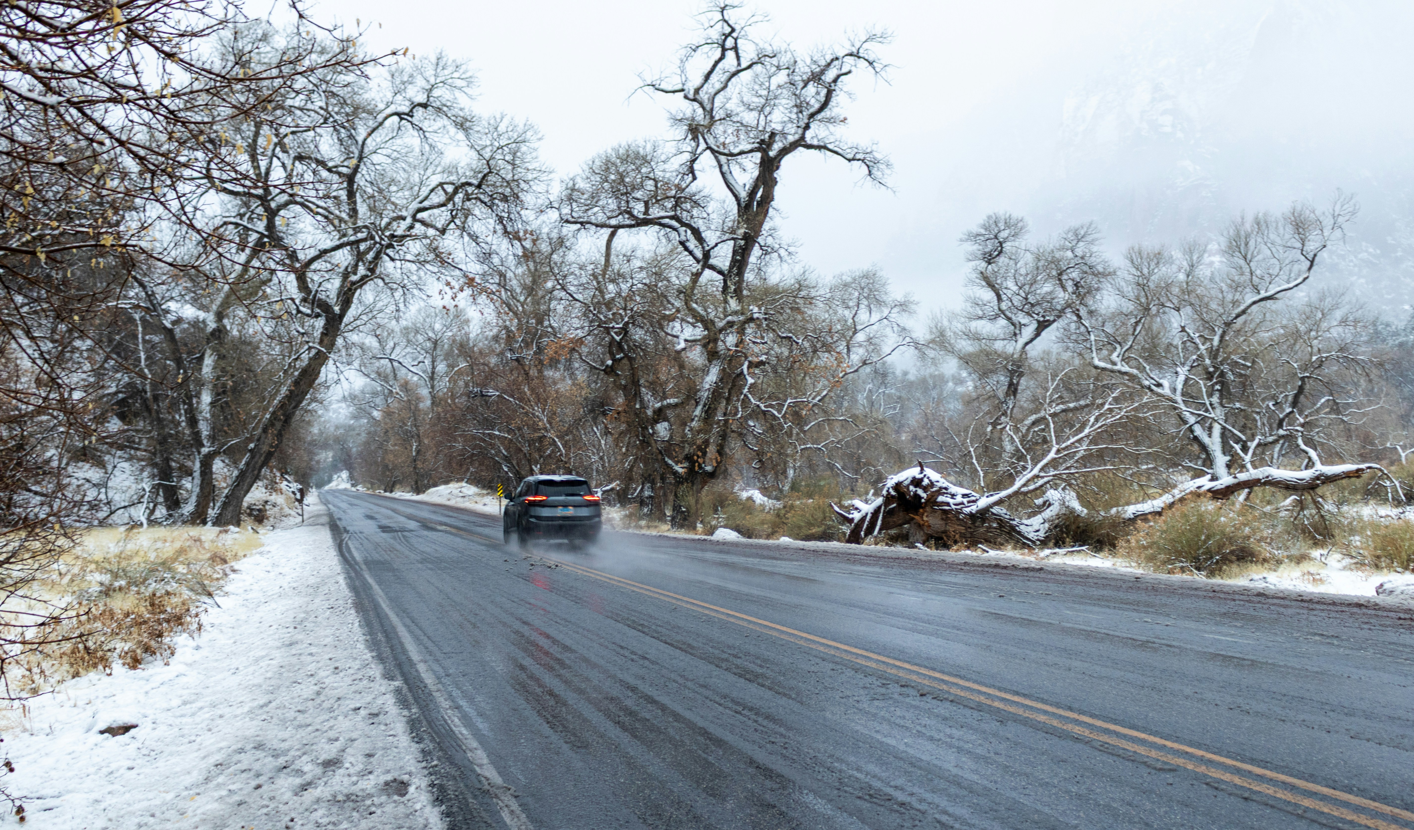 A car drives on a wet road in snowy weather.