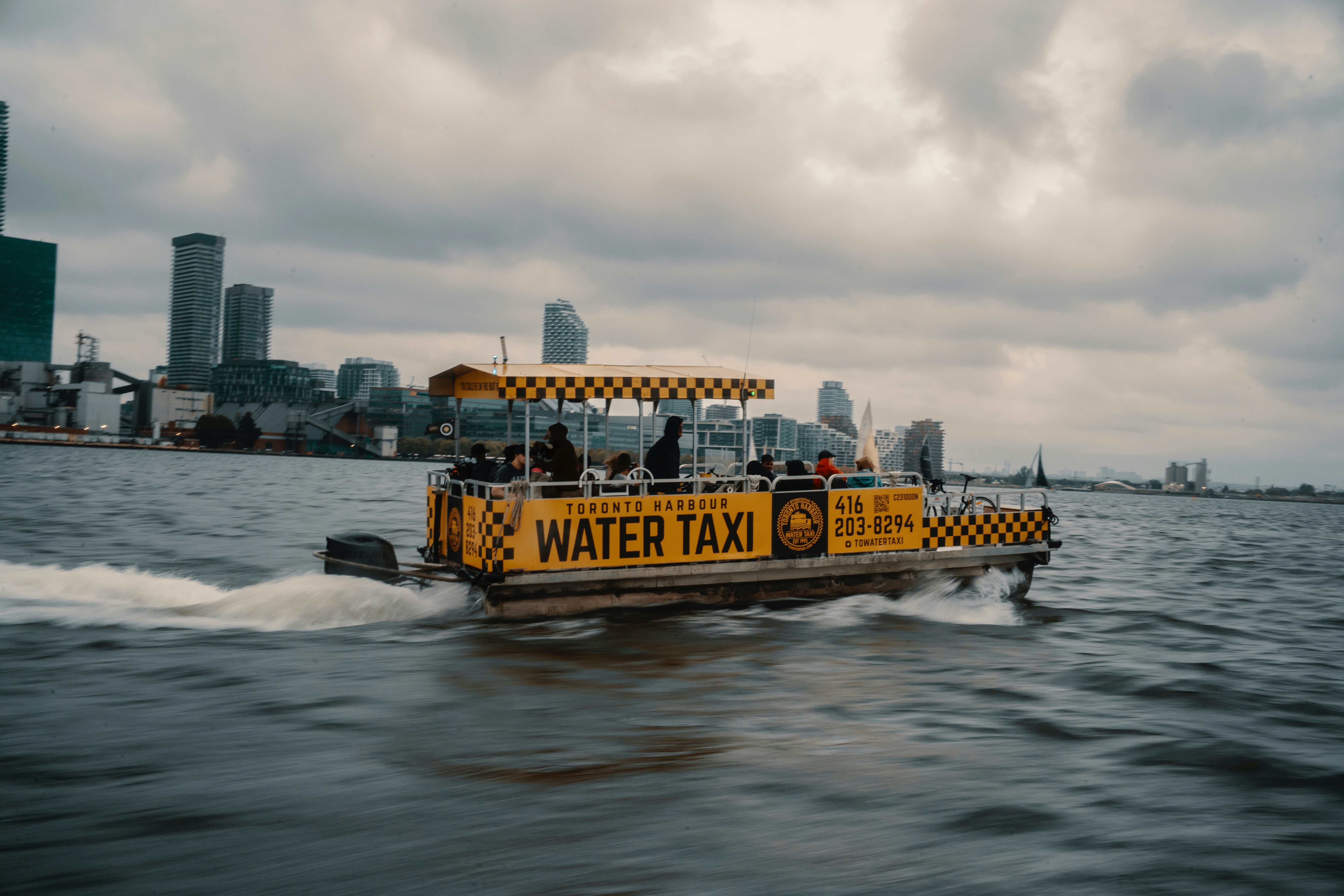 Yellow water taxi boat moving on water with city skyline.
