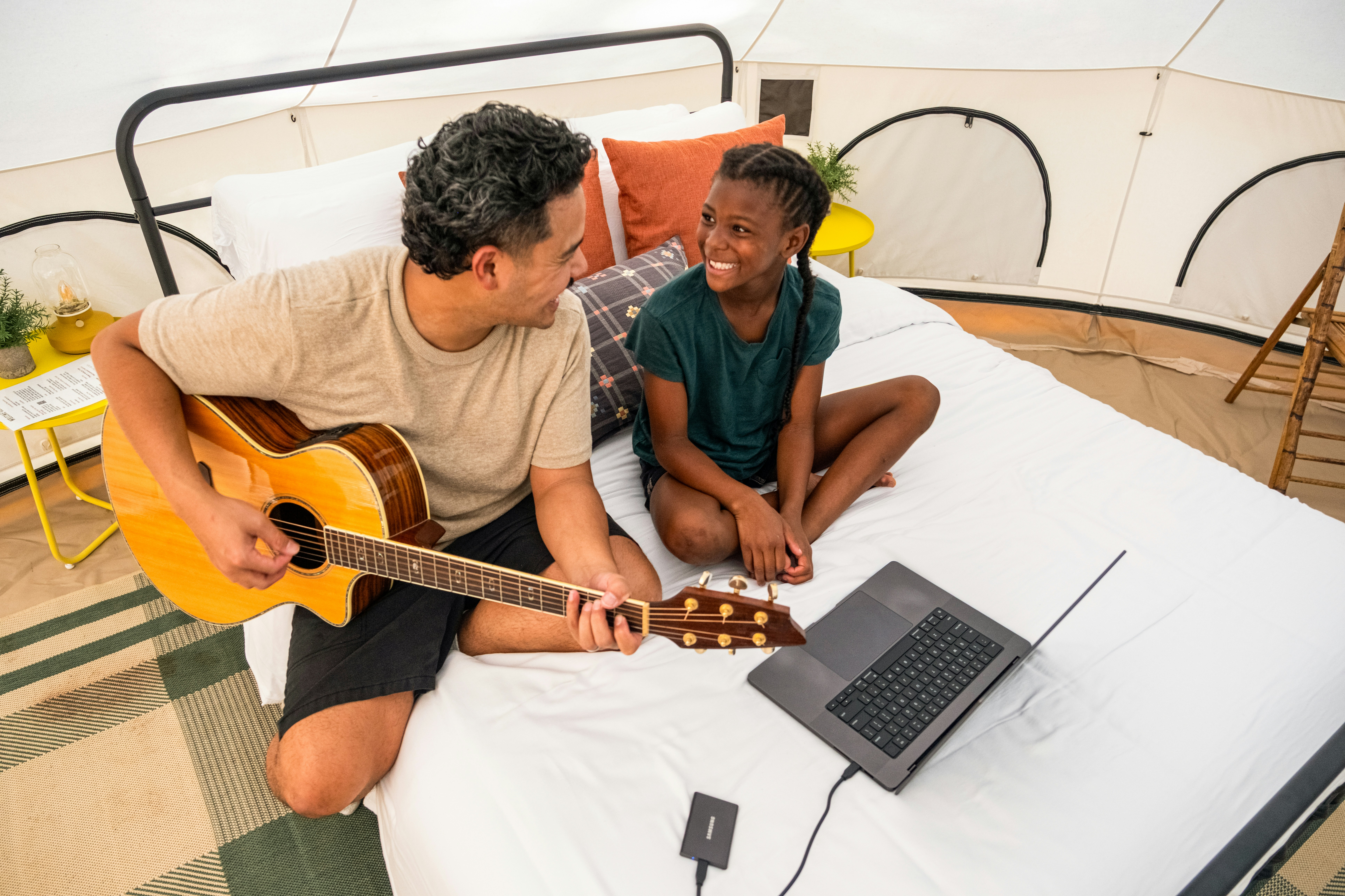 Man plays guitar for smiling girl on bed