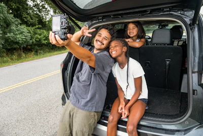 Father and daughters take a selfie by the car.