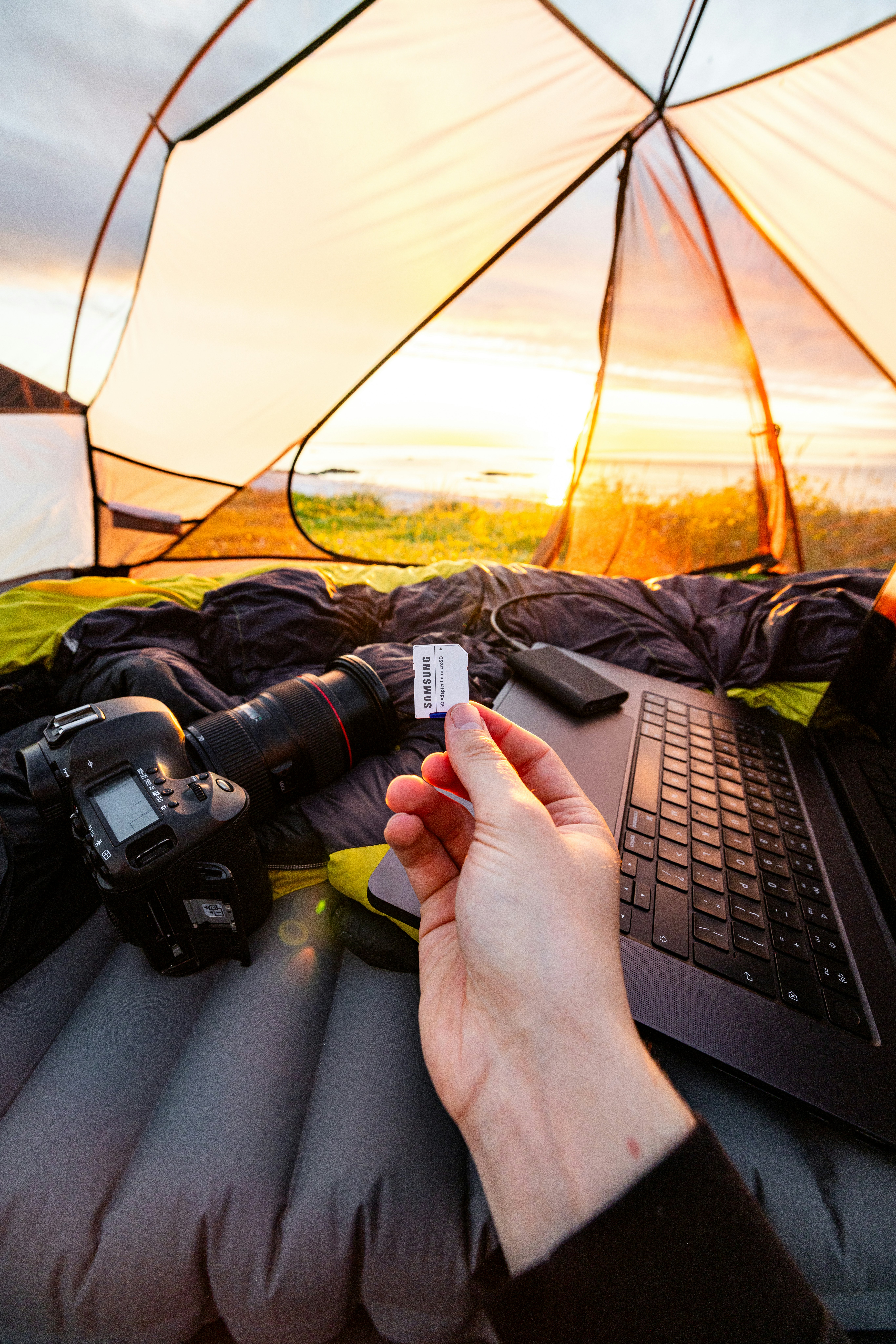 Hand holding sd card with camera and laptop inside tent