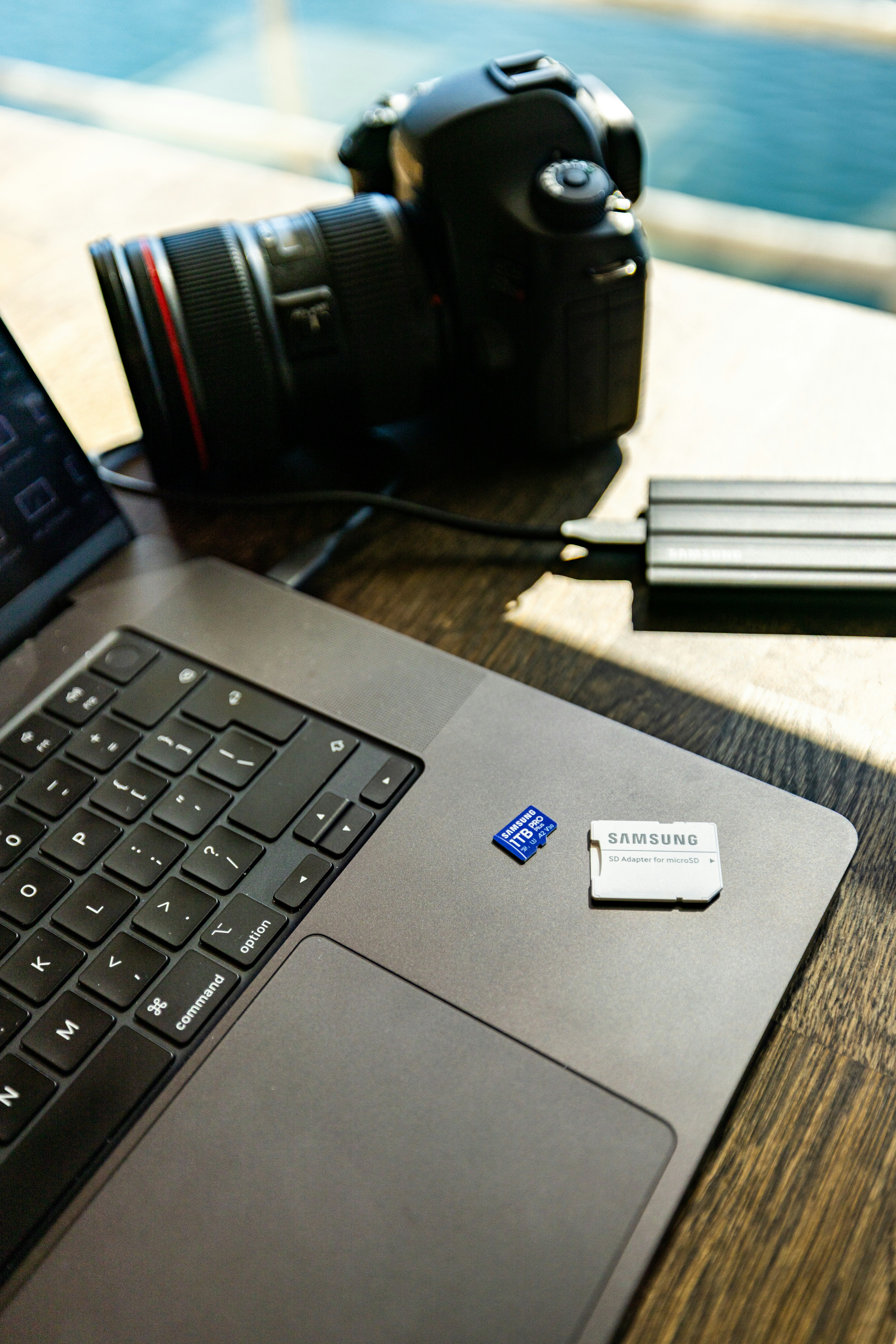 Laptop, camera, and storage devices on wooden table.