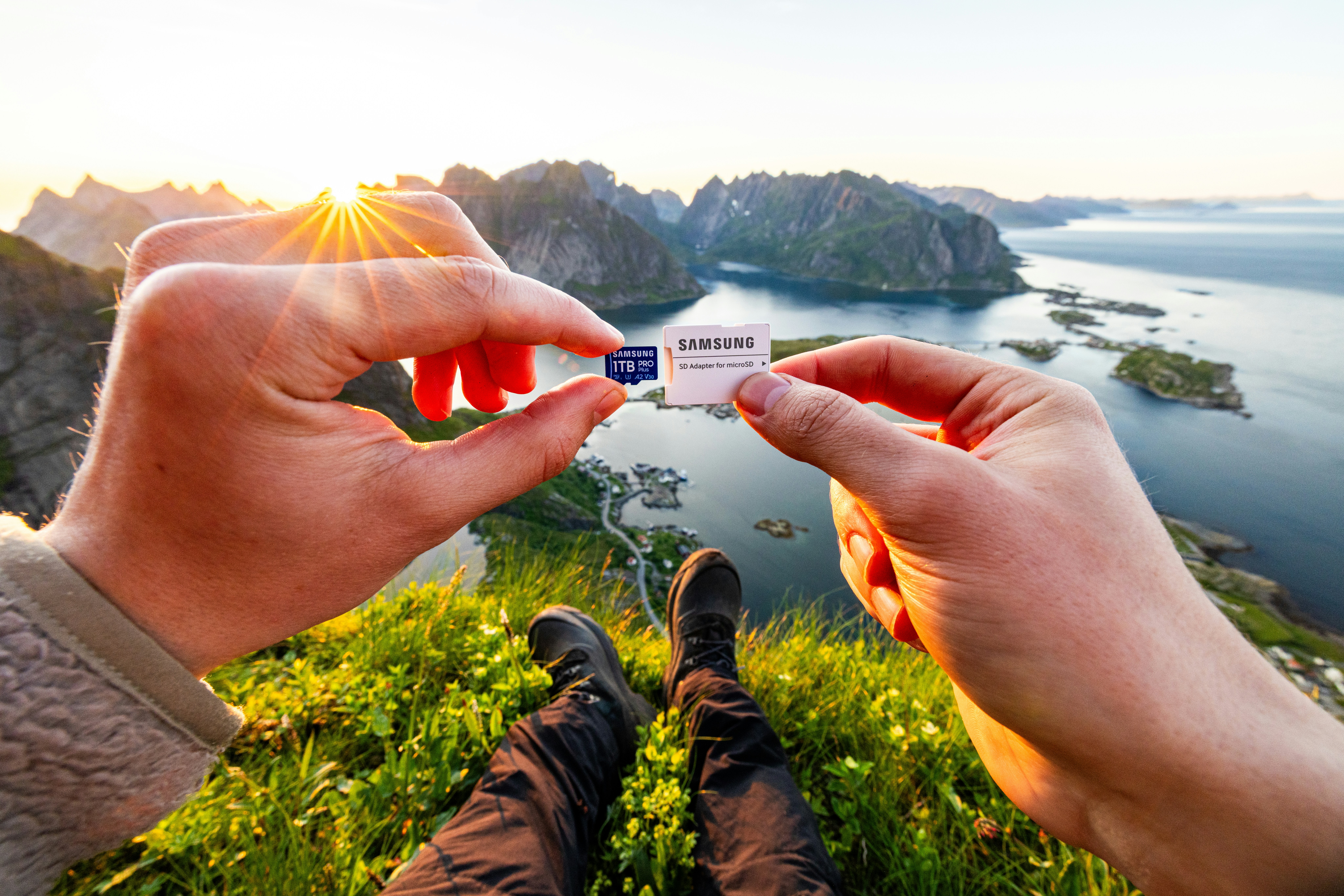 Hands hold sd card against scenic mountain and sea landscape.