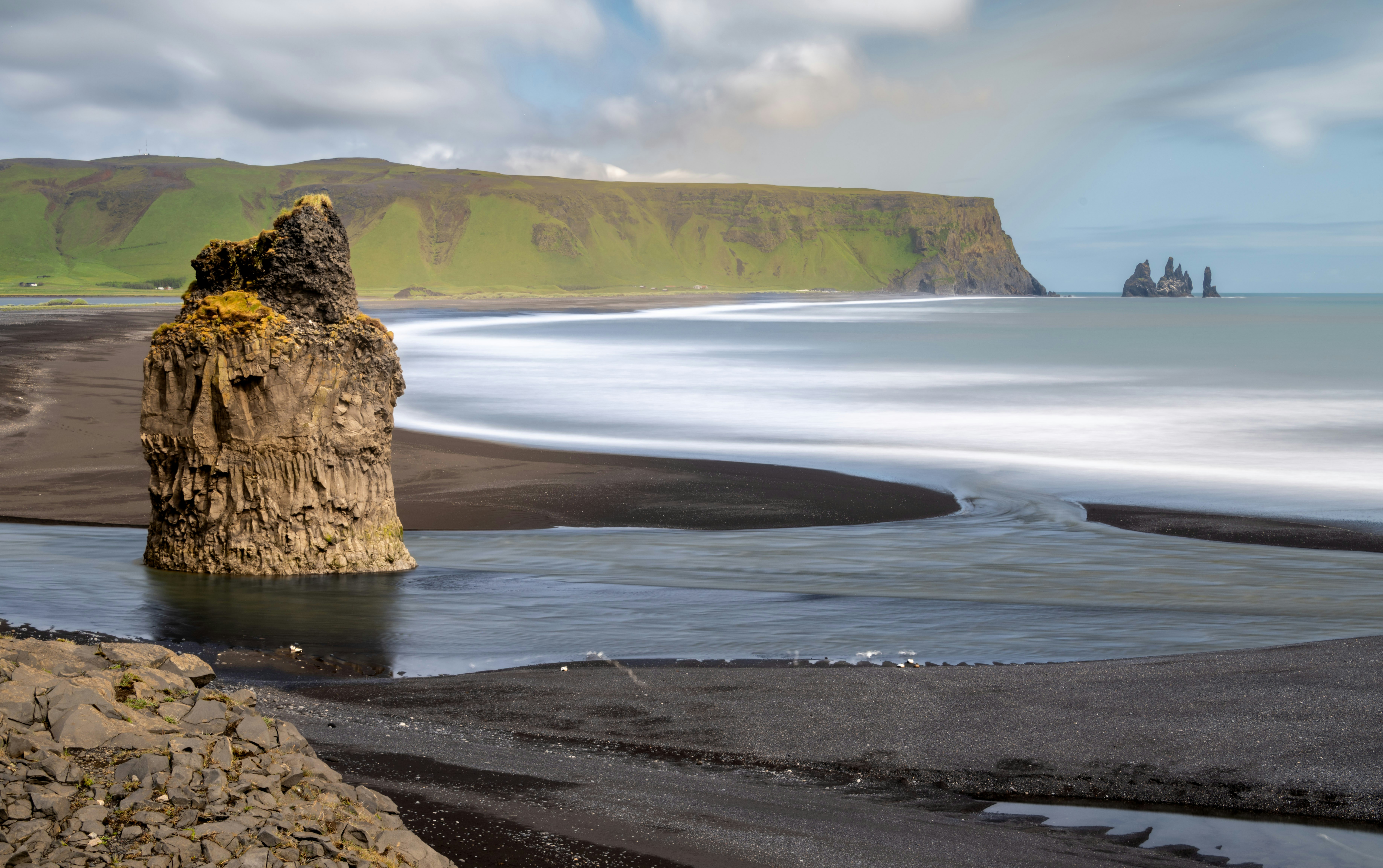 Black sand beach with rock formations and ocean waves.