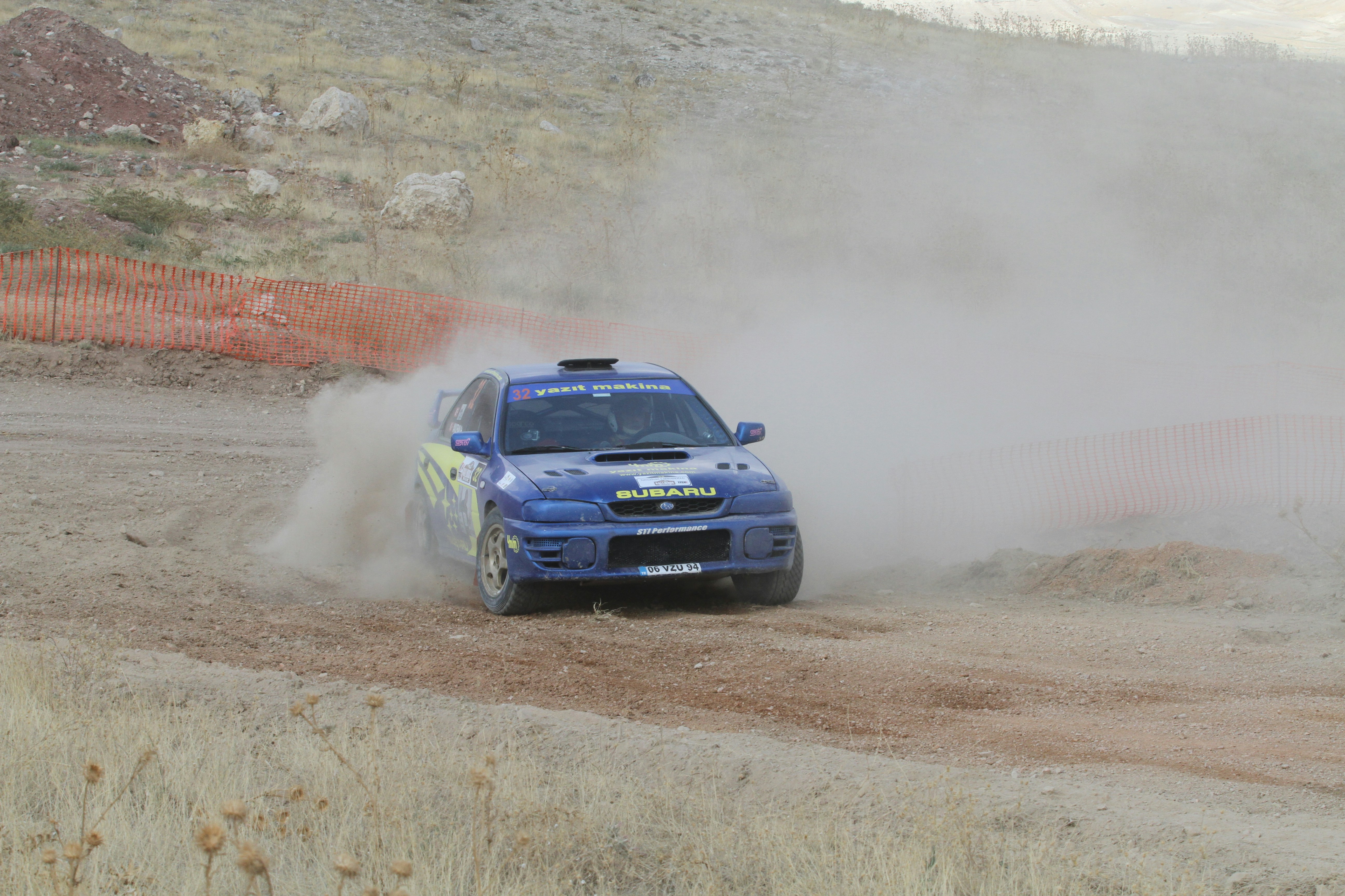 Blue rally car kicking up dust on a dirt track