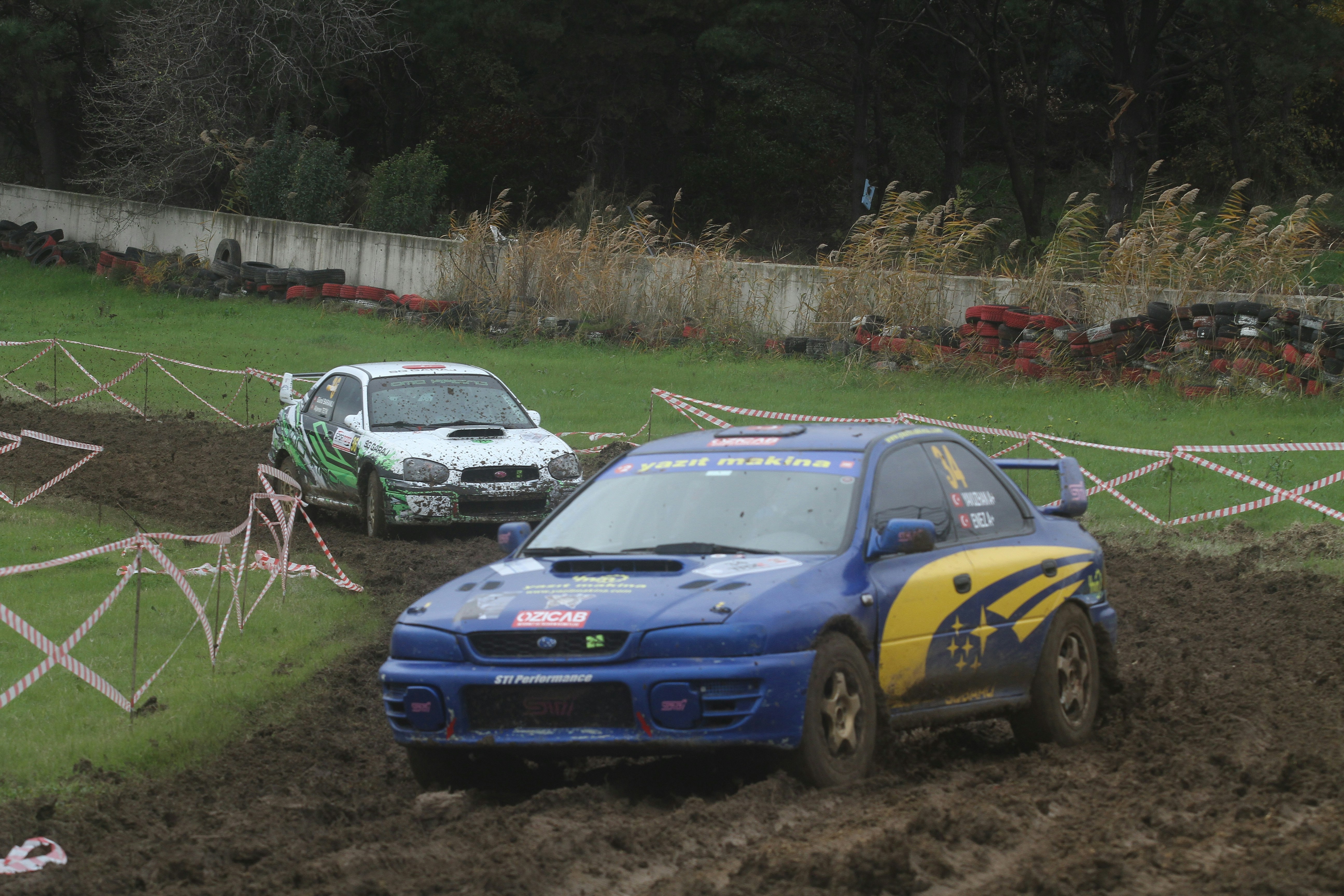 Two rally cars race on a muddy track.