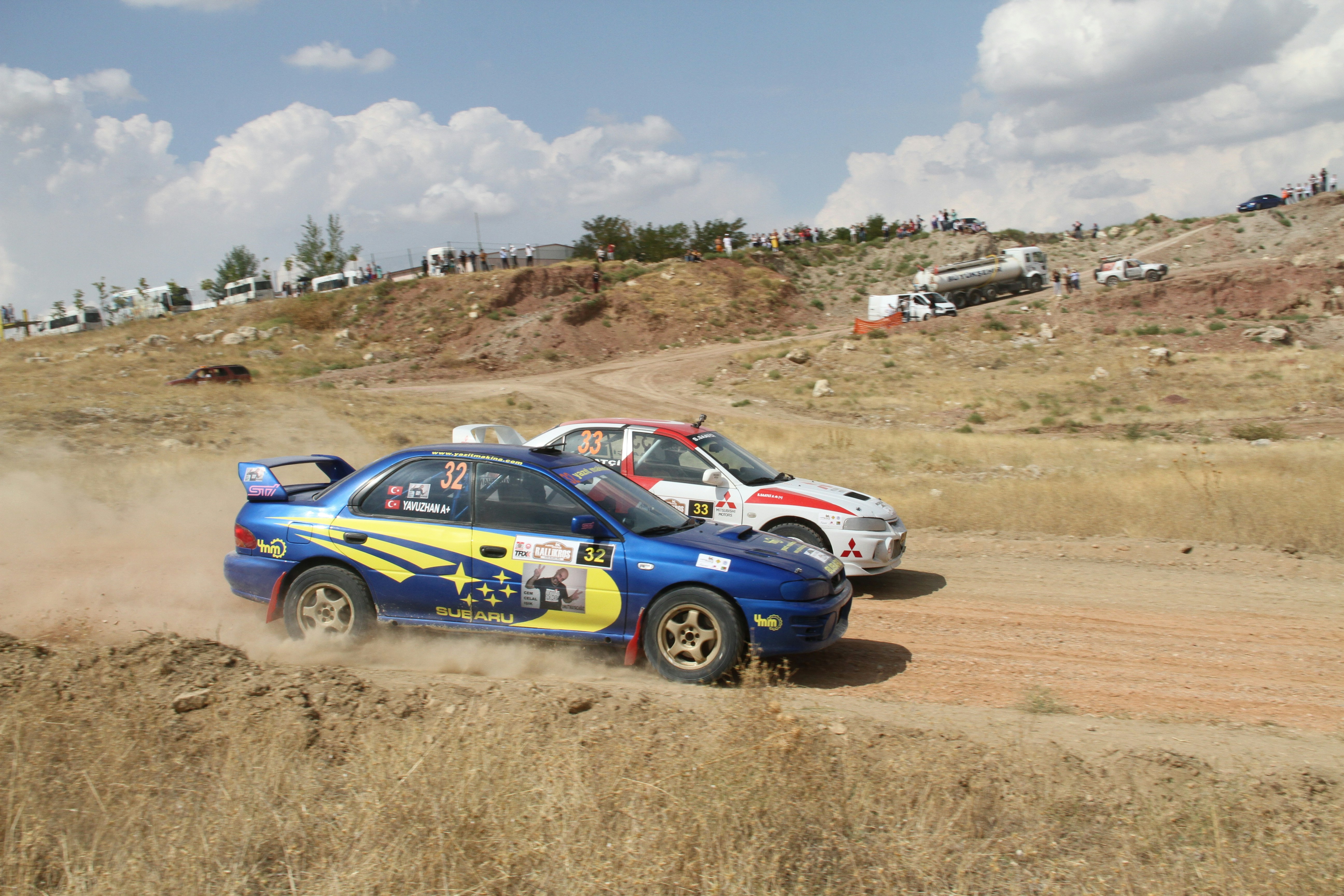 Two rally cars competing on a dusty dirt track.