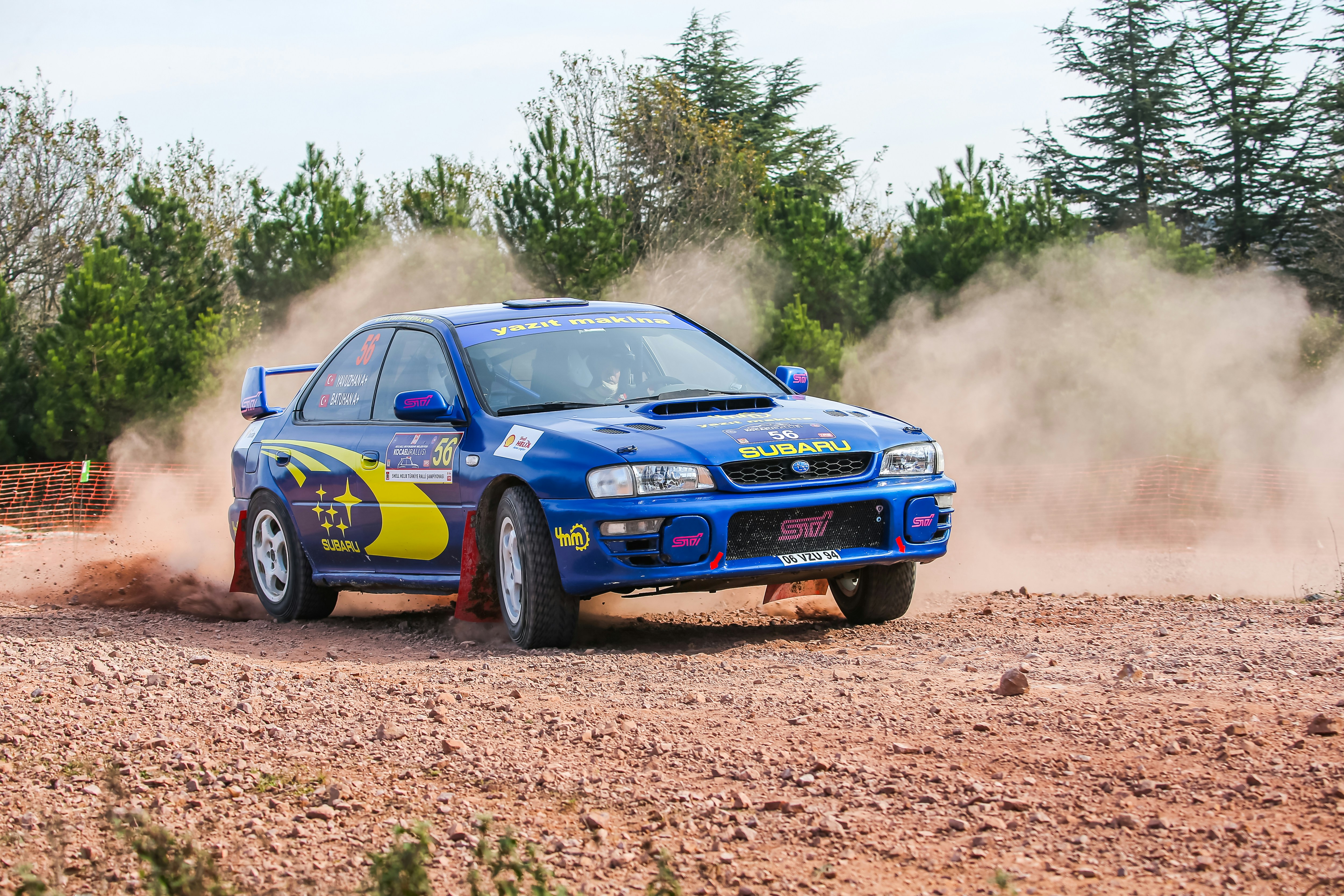 Blue rally car kicking up dust on a dirt track