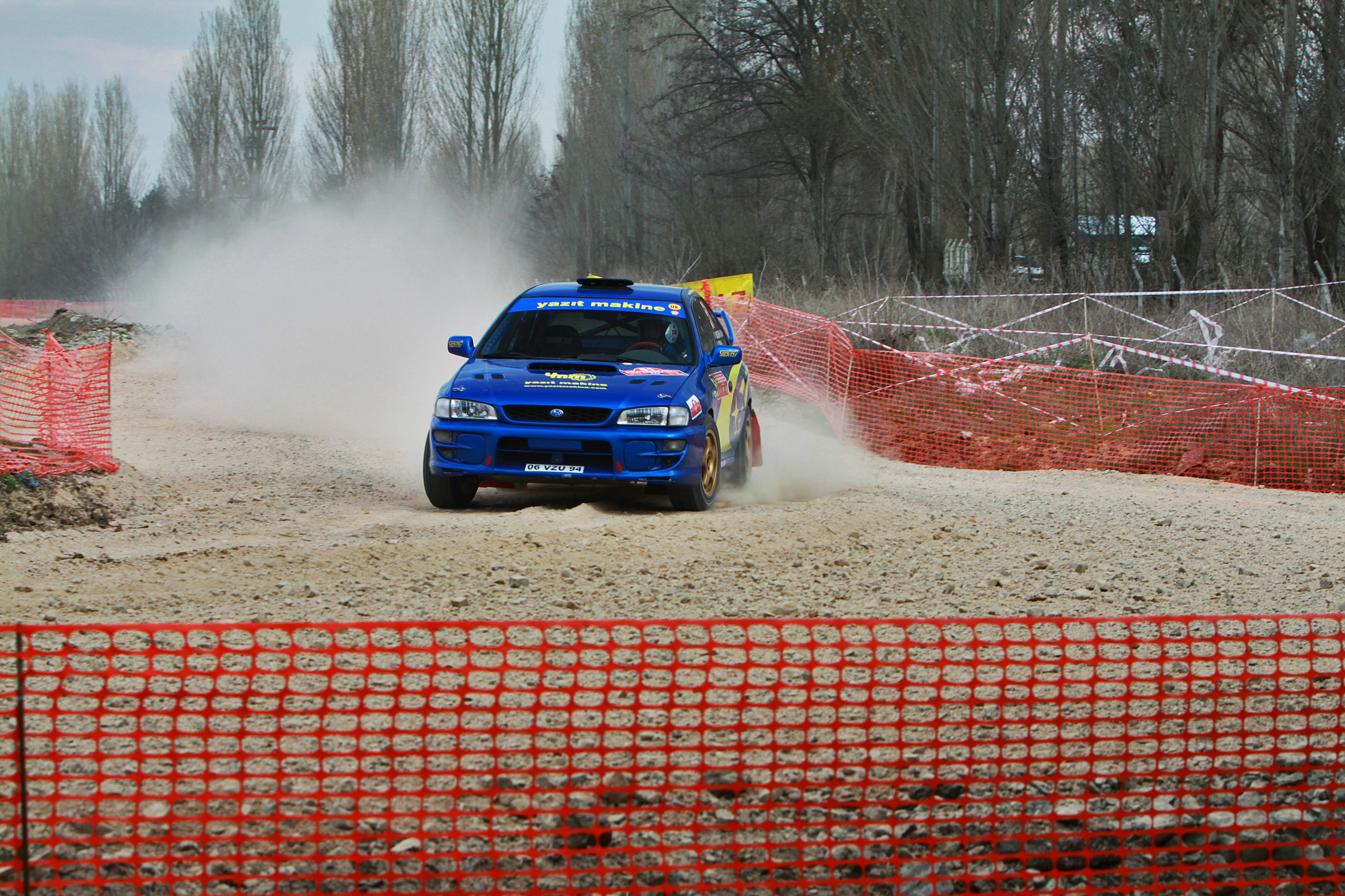 Blue rally car kicking up dust on dirt track
