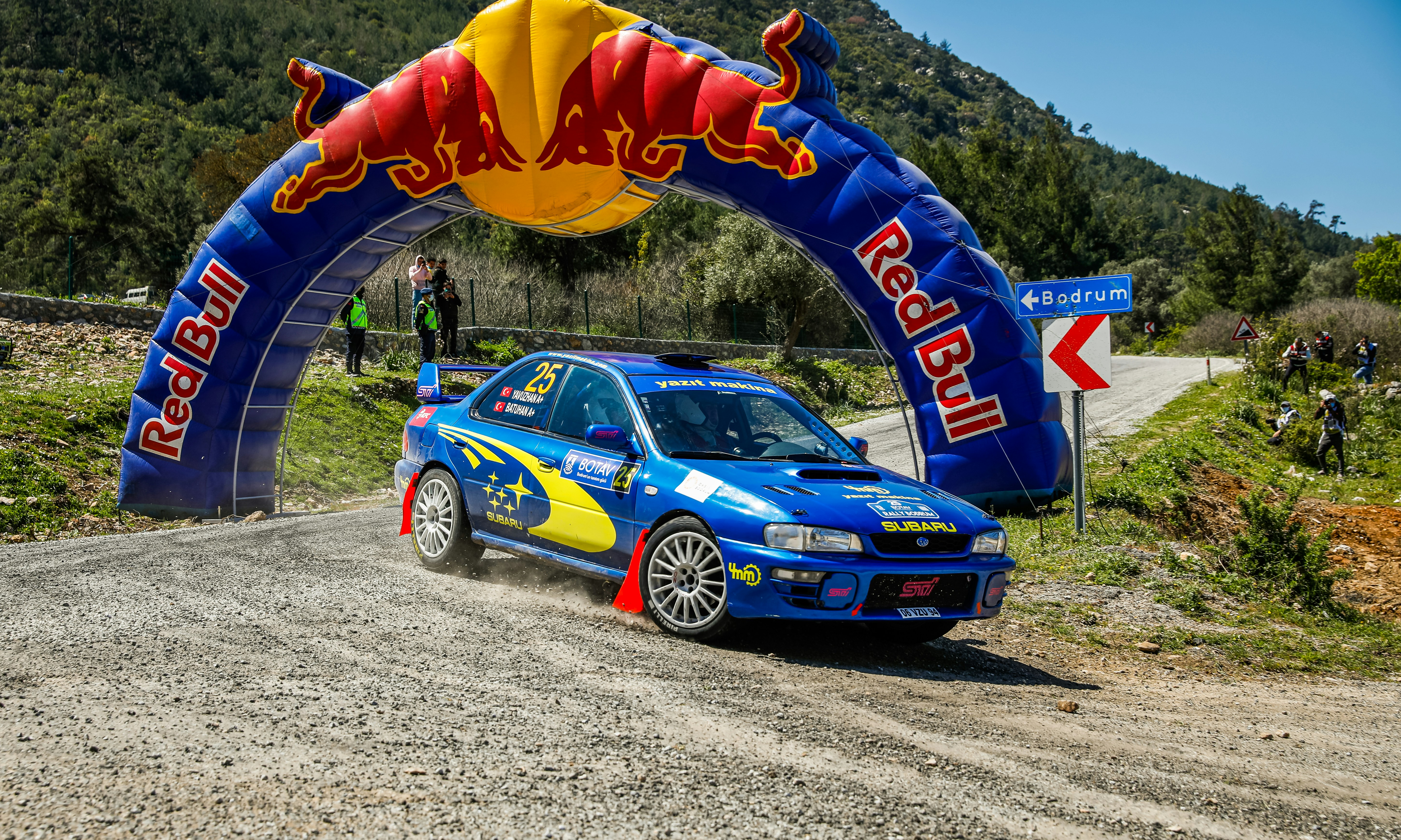 Blue rally car drives through red bull arch.