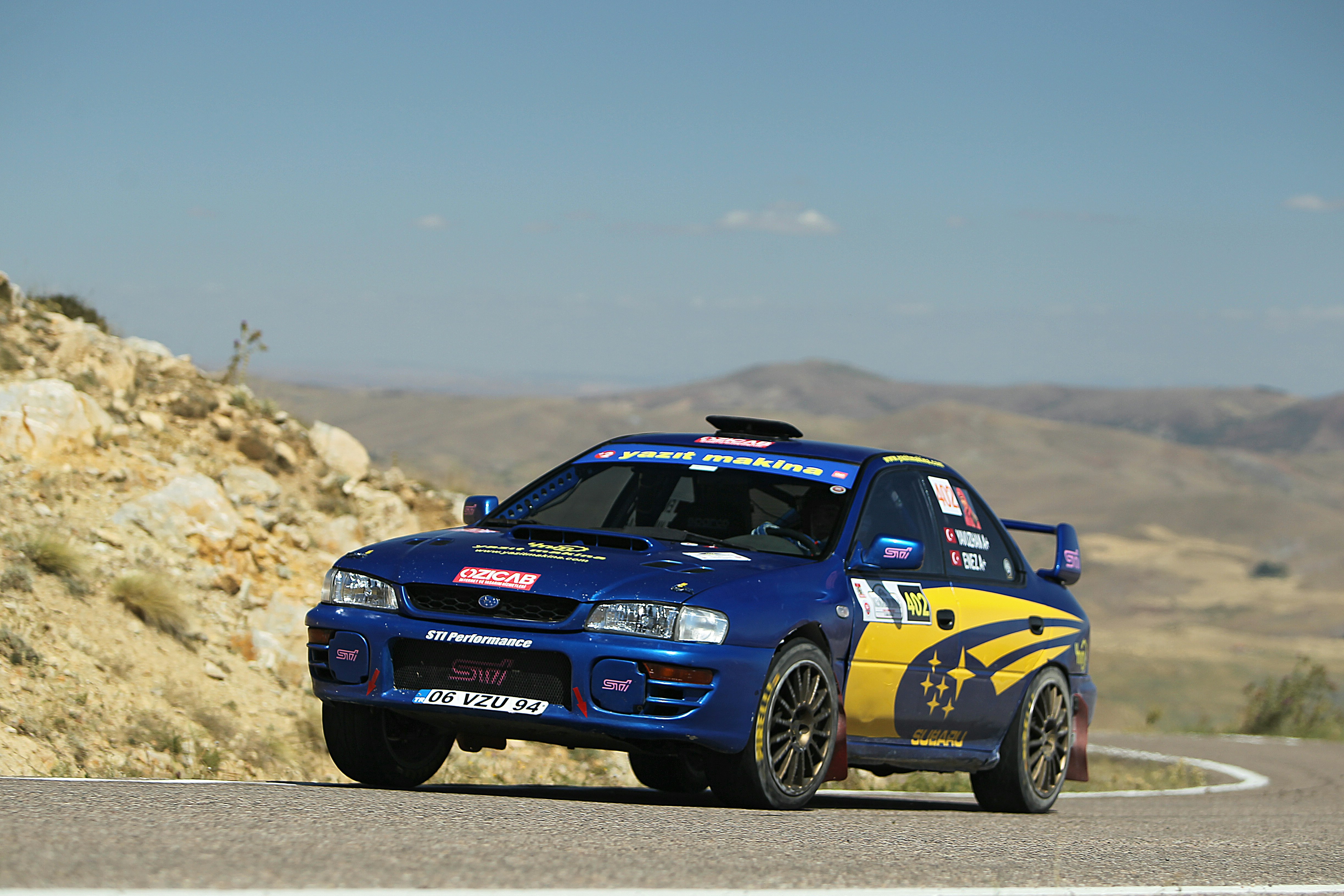 Blue rally car speeding on a winding mountain road.