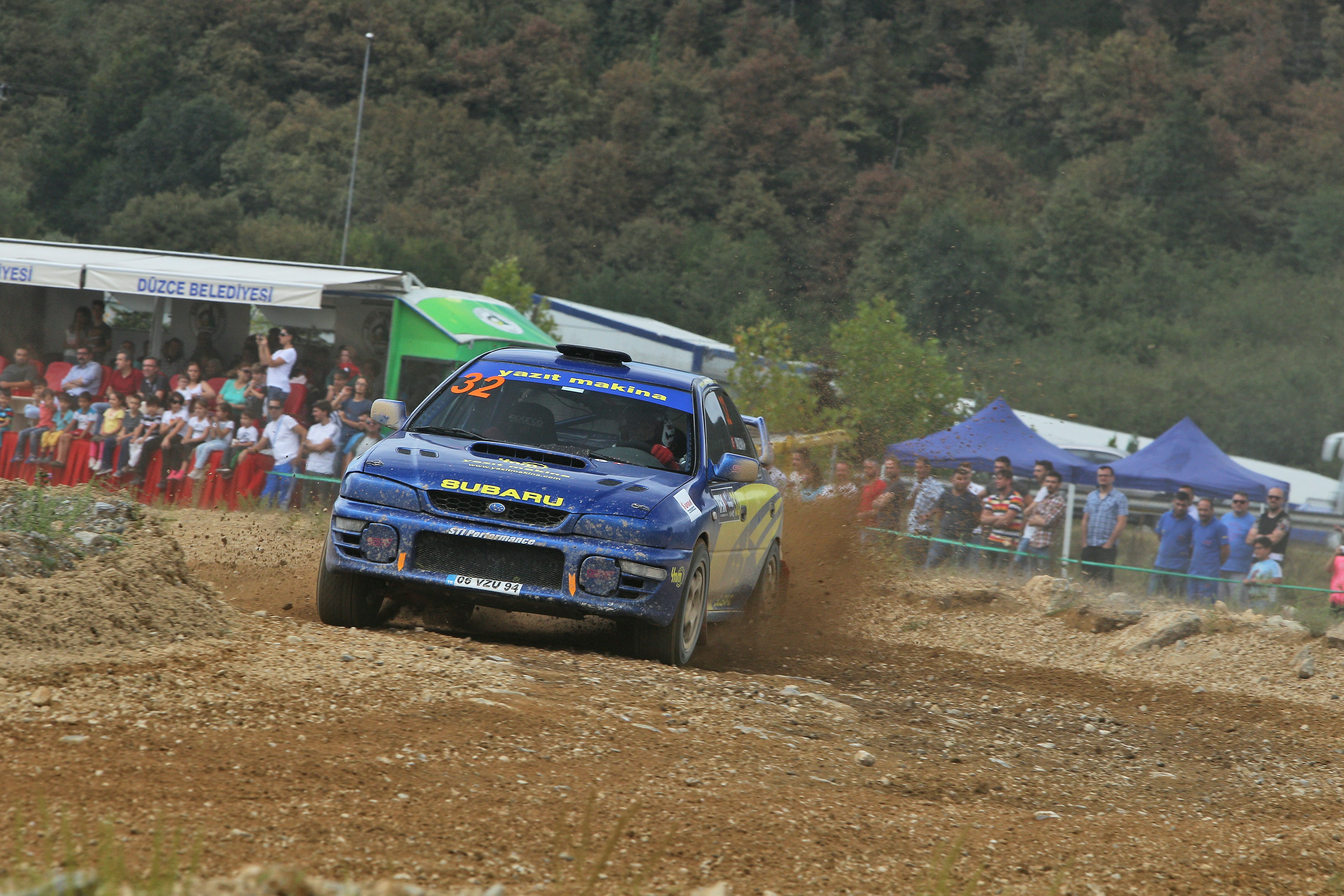 Blue subaru rally car kicking up dirt on track.
