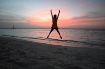 Silhouette of person jumping on beach at sunset