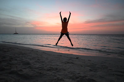 Silhouette of person jumping on beach at sunset