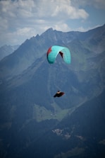Paraglider soaring over majestic, forested mountains.