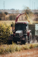 Red tractor harvesting crops into trailer