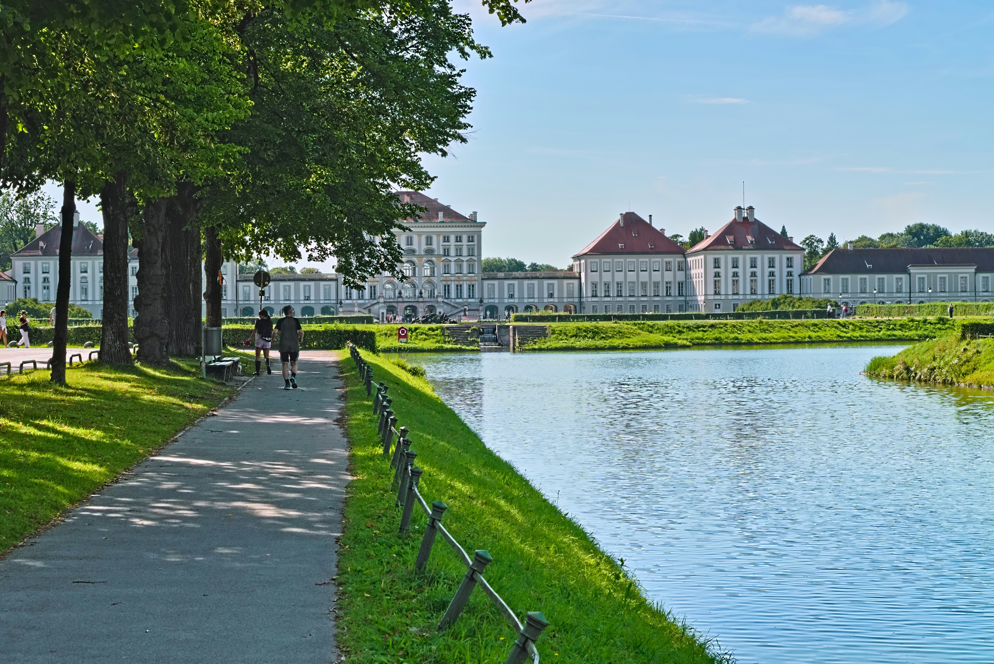 People walk on a path beside a lake with a palace.