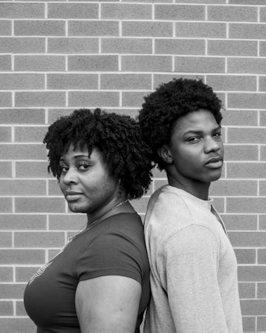 Two people stand back to back against a brick wall.