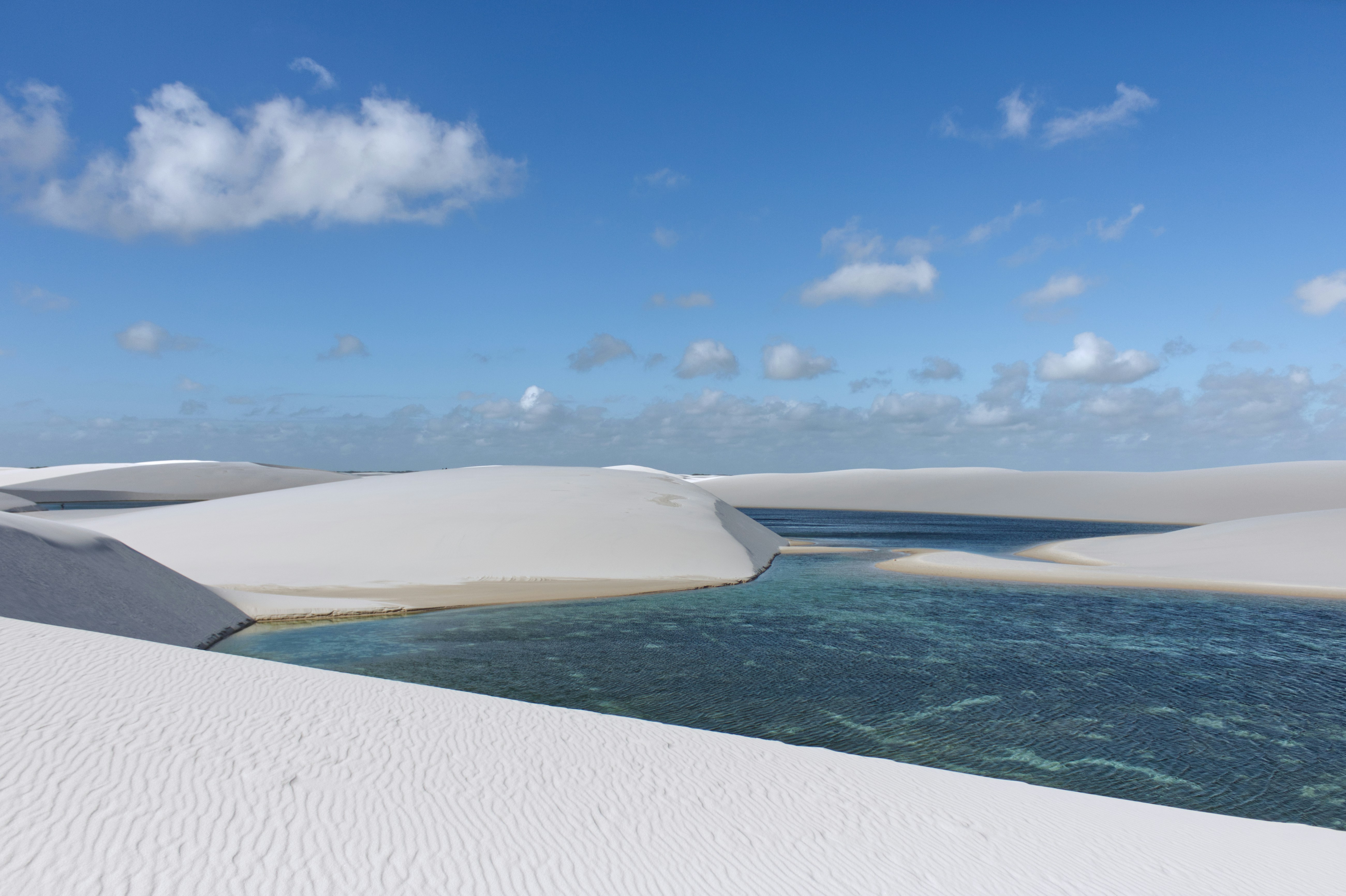 Weiße Sanddünen mit blauem Wasser unter bewölktem Himmel