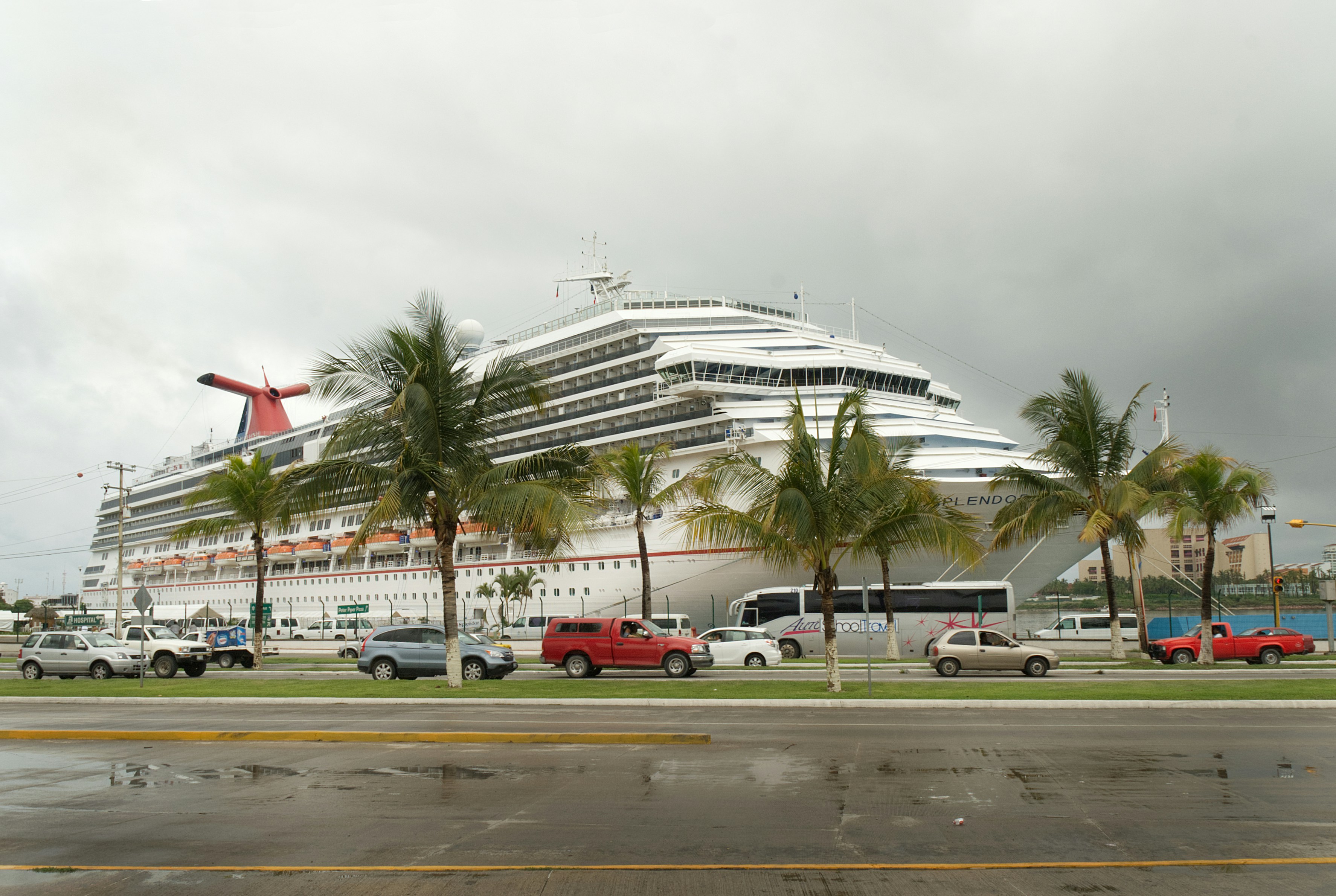 Large white cruise ship docked with palm trees and vehicles.