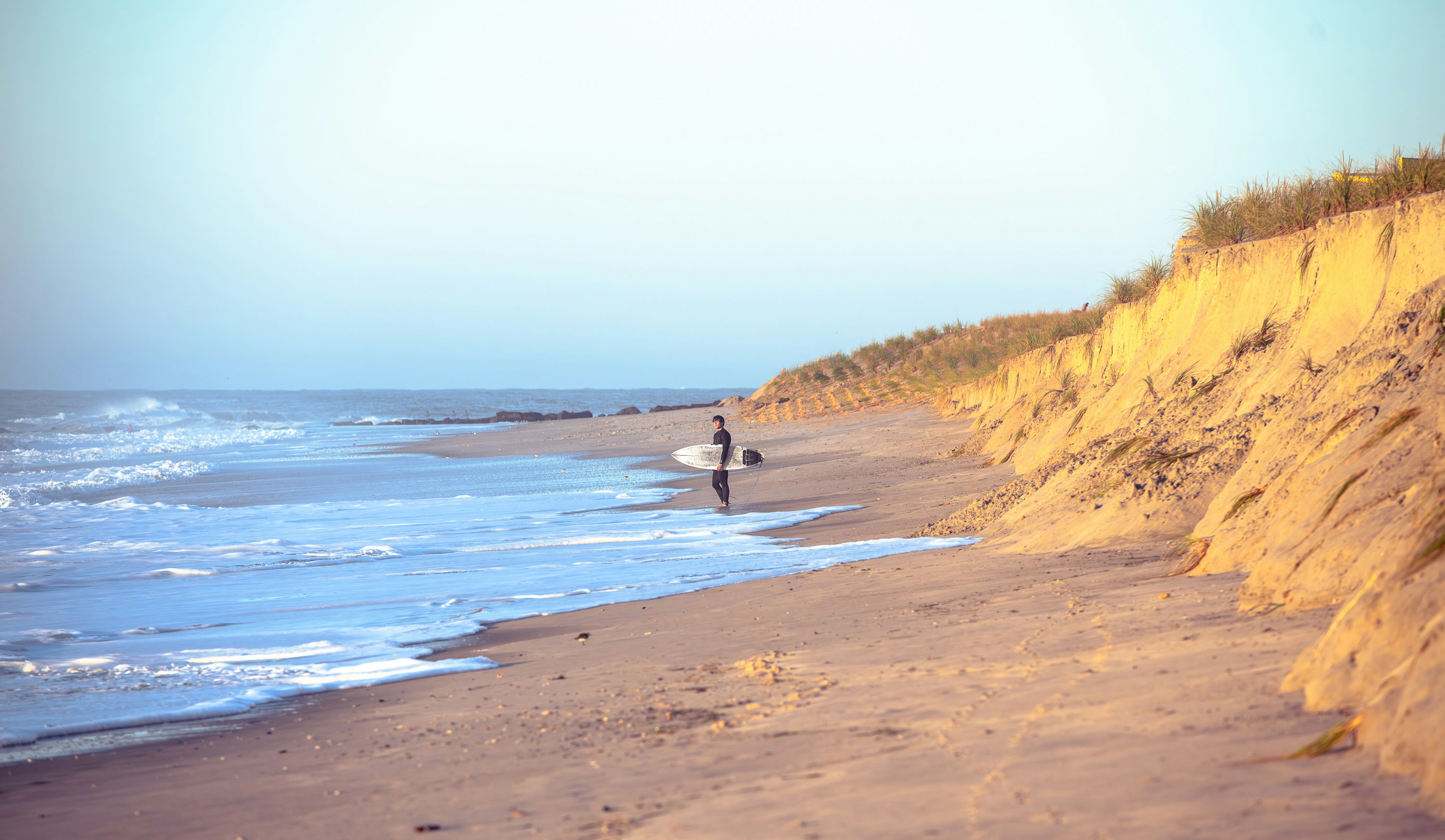 Person walking on a sandy beach with surfboard