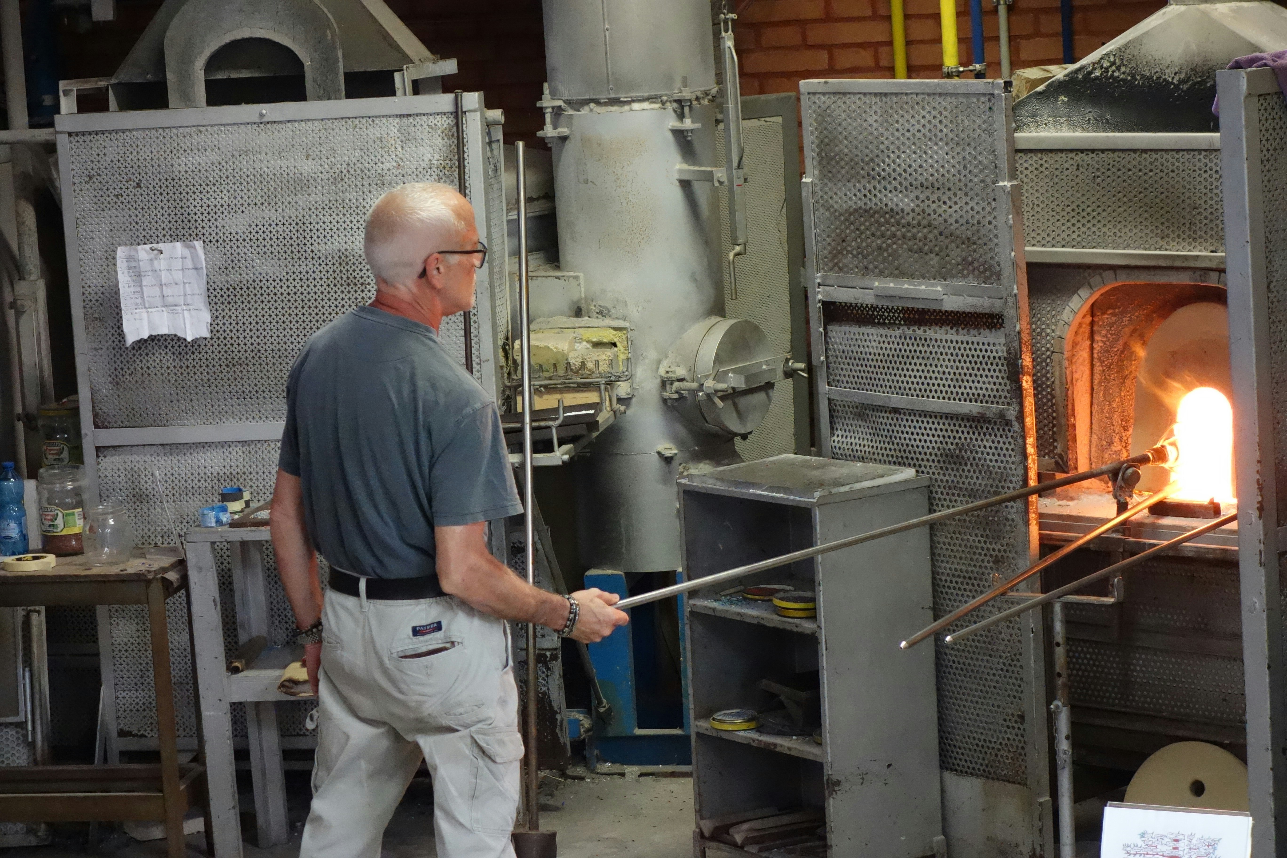 Glassblower works with molten glass in a furnace.