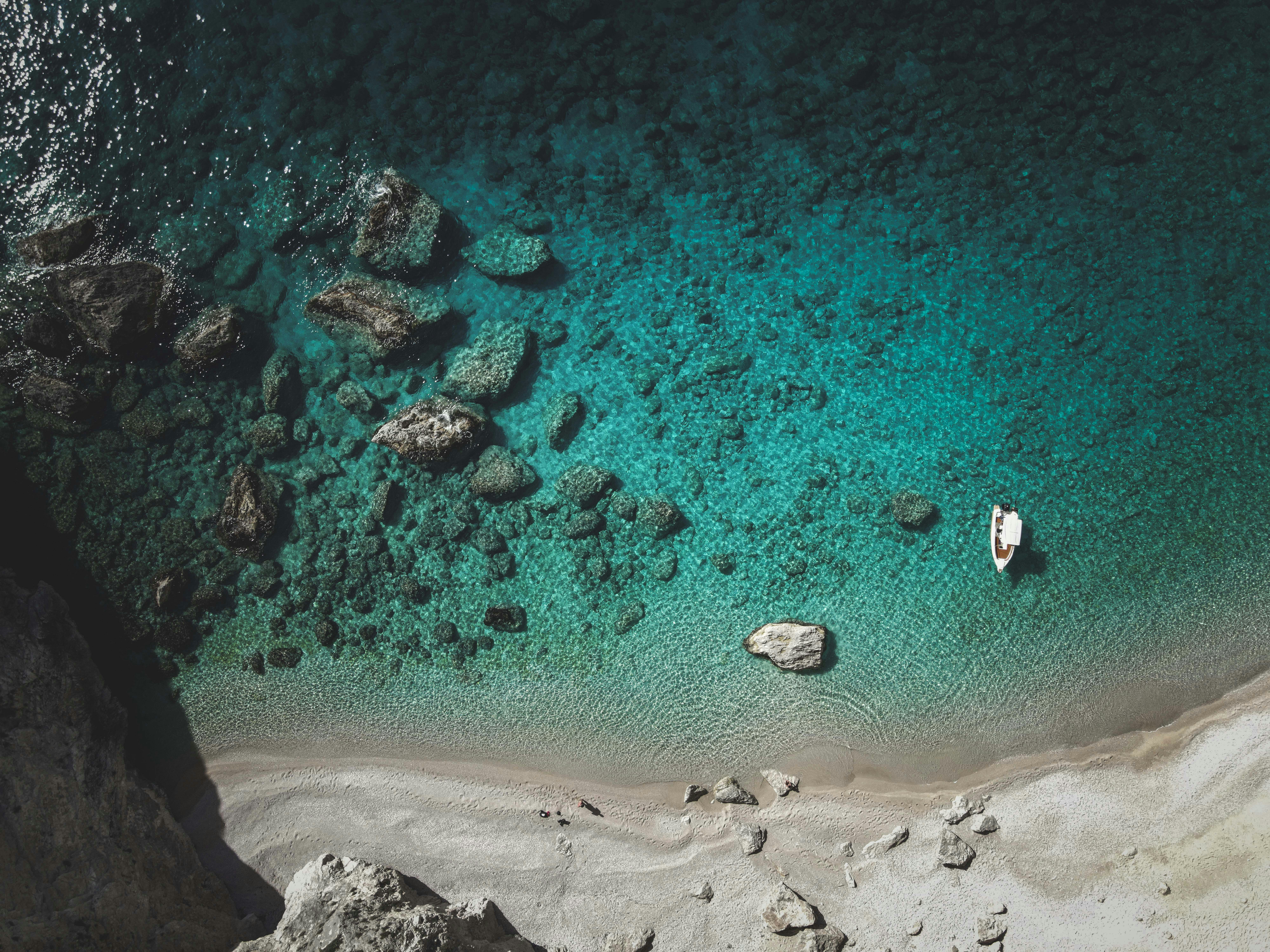 작은 보트가 바위 해안 근처의 맑은 청록색 바다에 떠 있습니다.