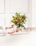 Hands exchanging a bouquet of yellow and orange flowers.