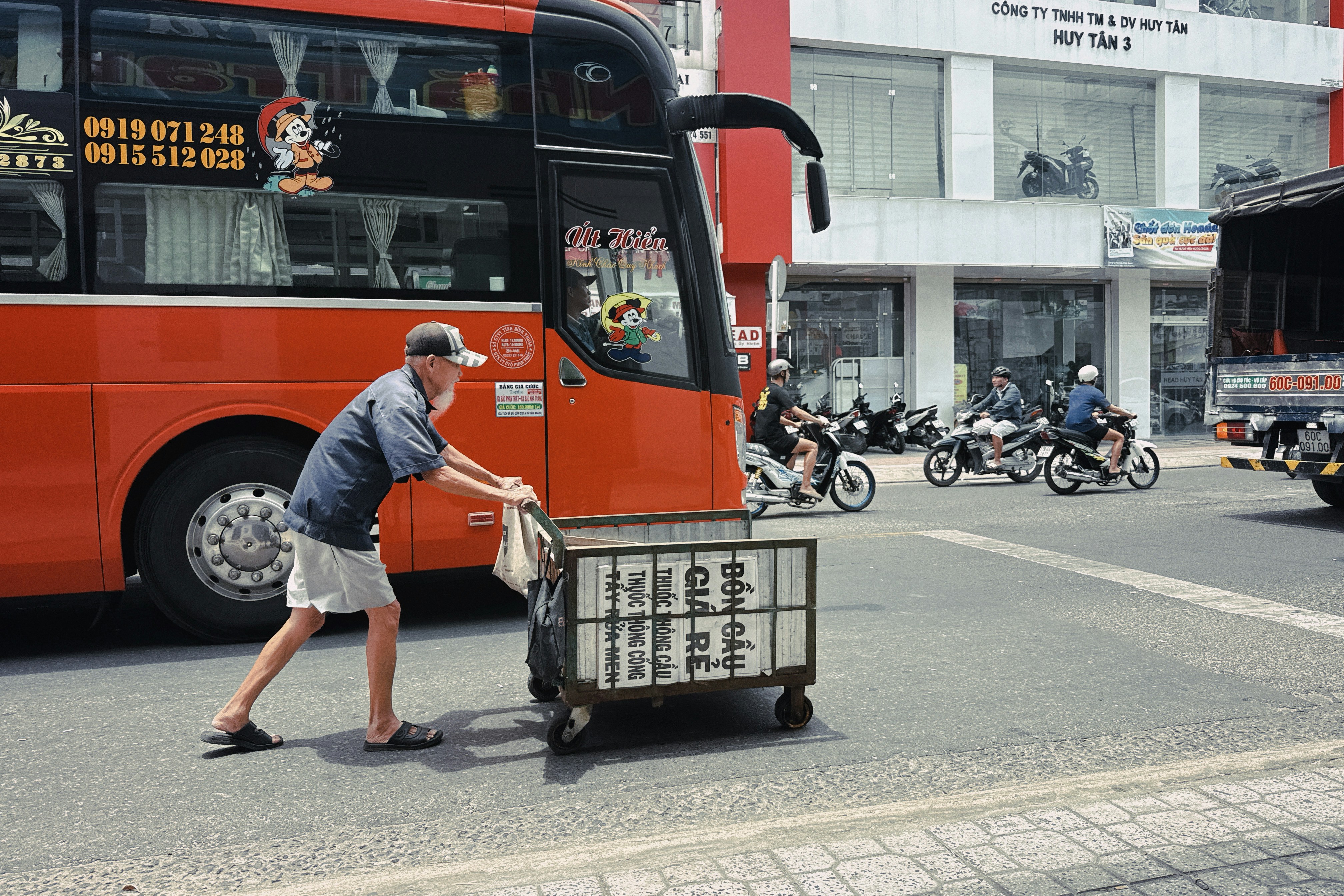 Мужчина толкает тележку рядом с большим оранжевым автобусом.