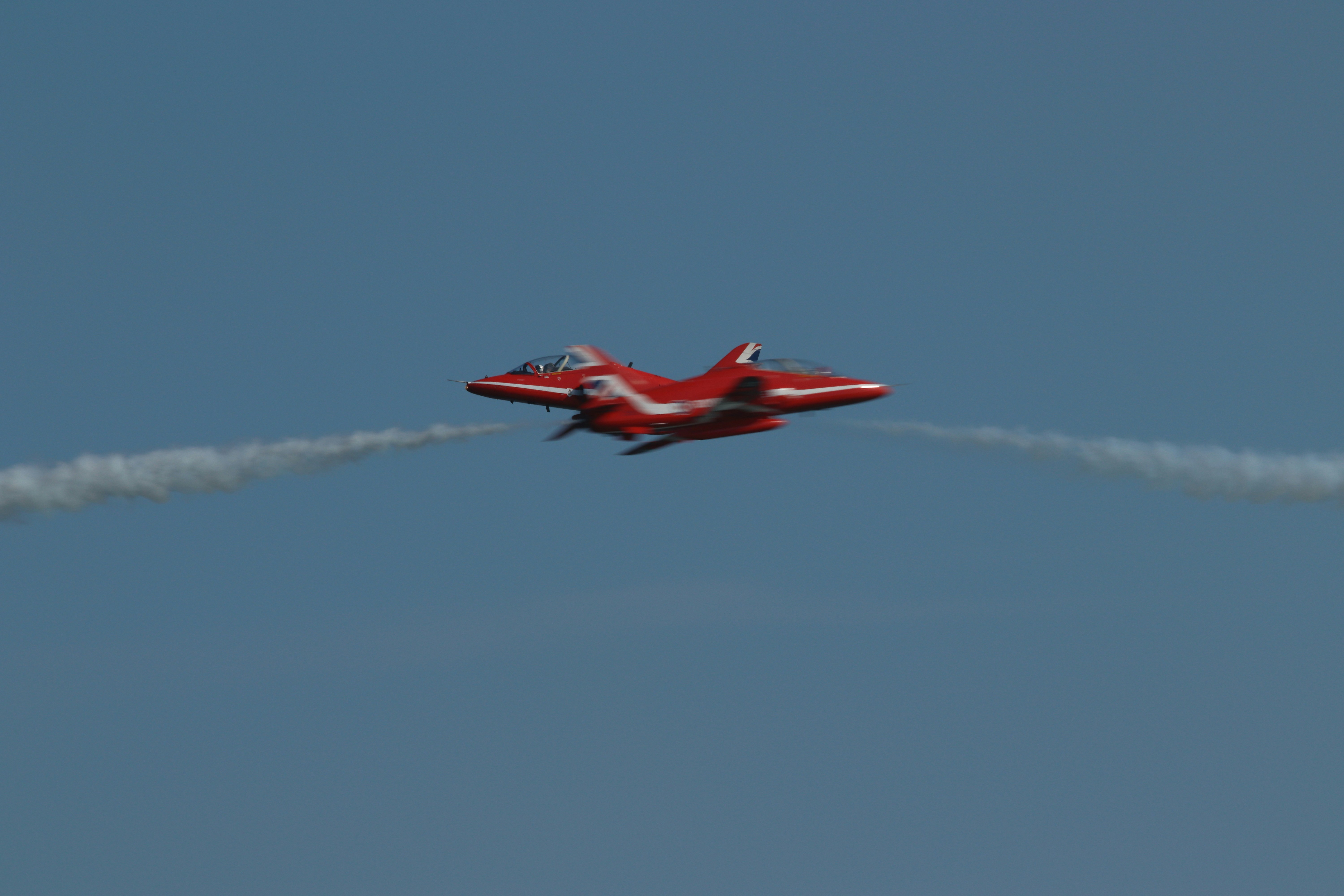 Red jet aircraft performing aerobatics with smoke trails.