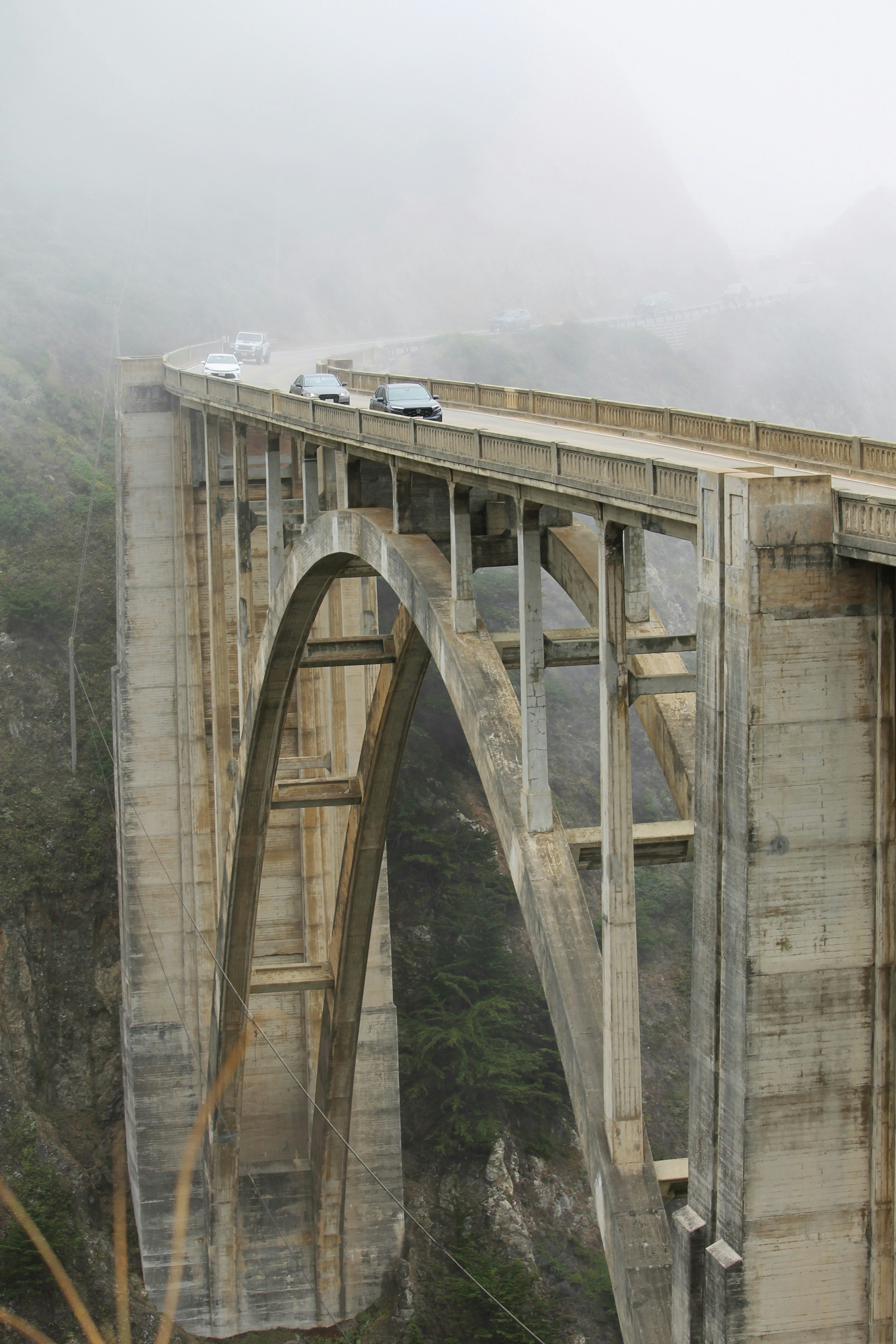 Cars driving on a foggy bridge over a canyon.