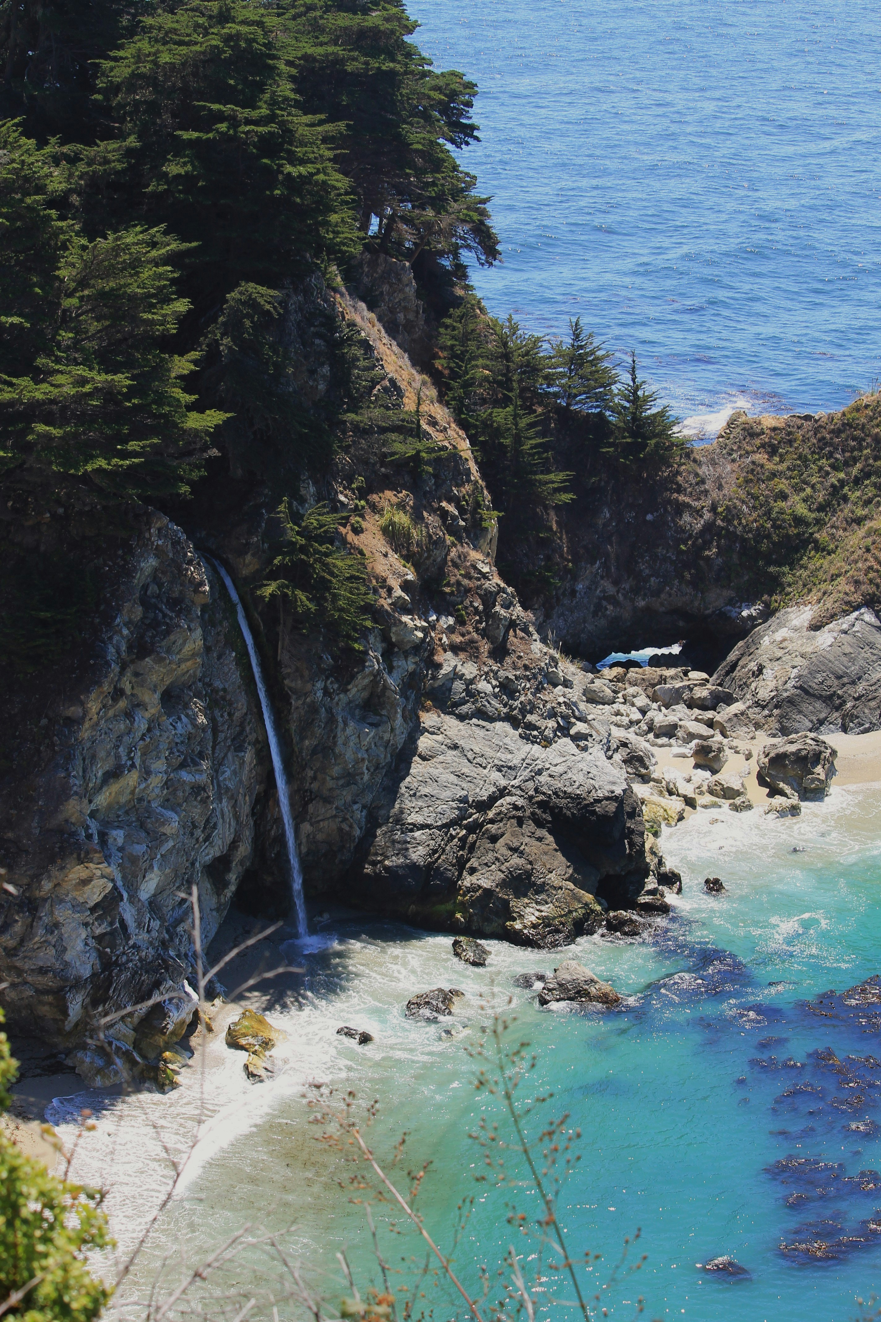Waterfall cascading onto a sandy beach by the ocean.