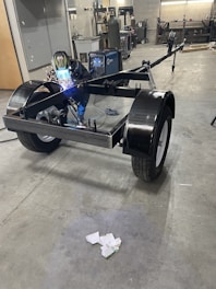 Welder working on a trailer frame in a workshop.
