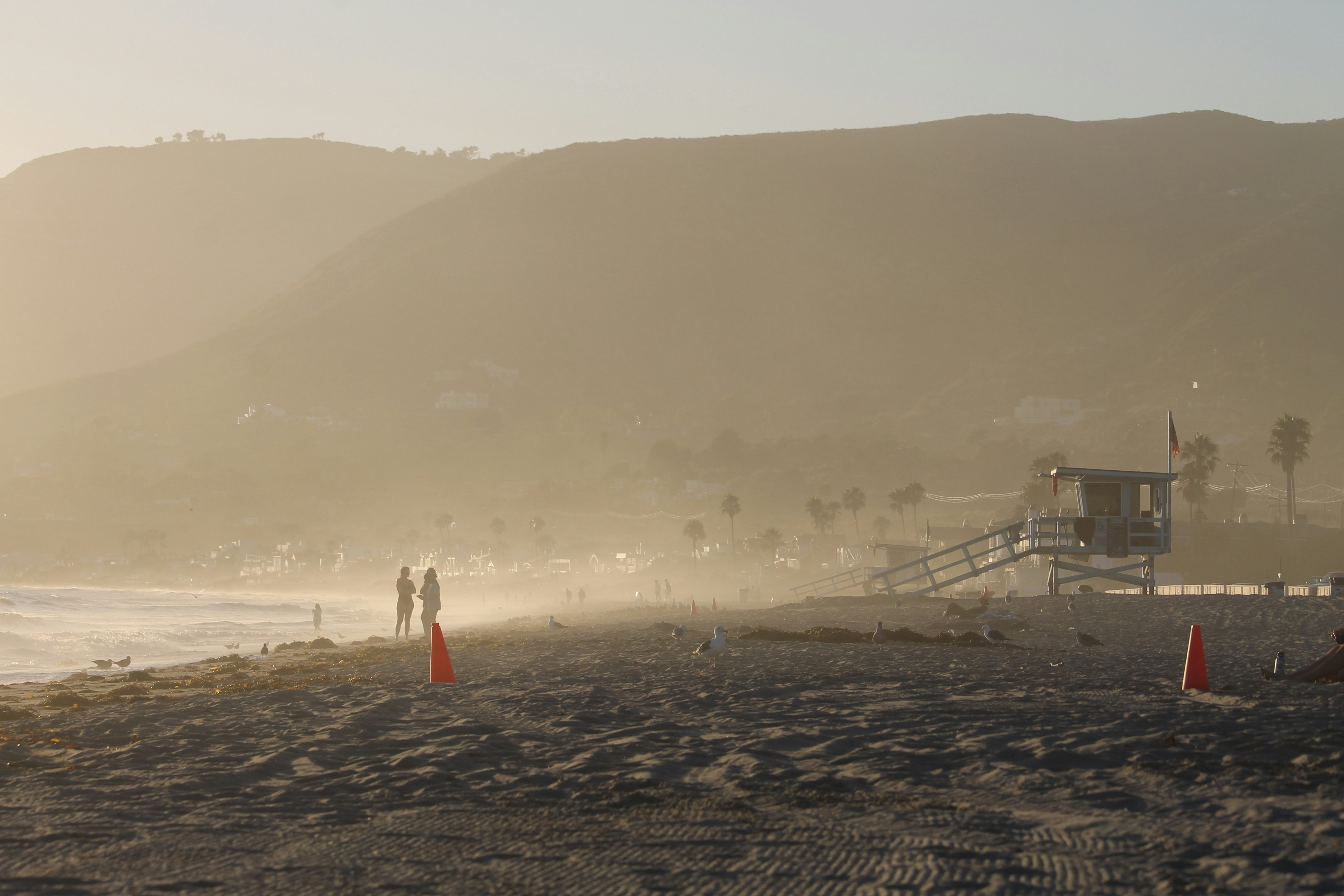 Beach with lifeguard tower and distant mountains at sunset.