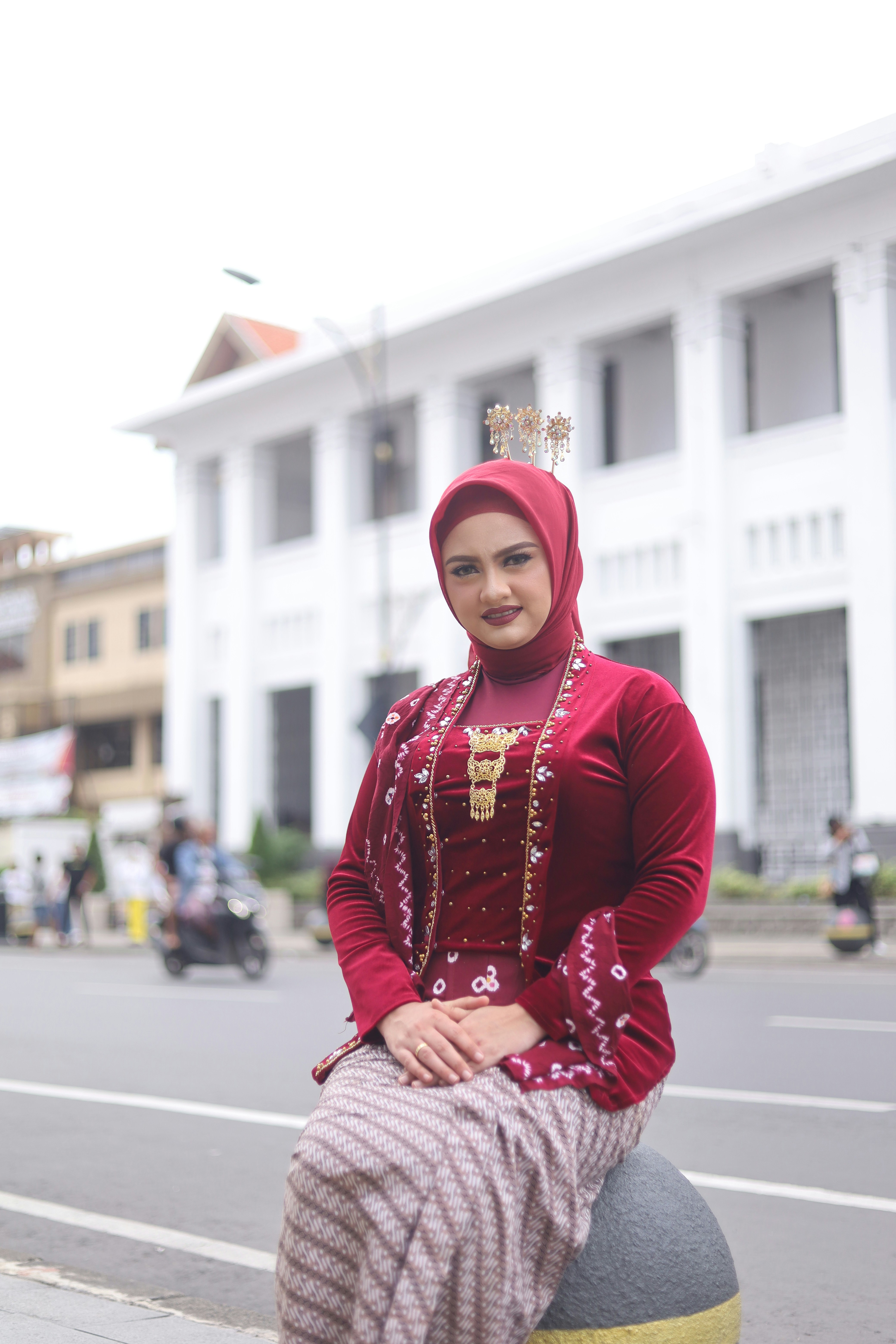 Wanita dengan pakaian merah tradisional dan jilbab duduk di luar