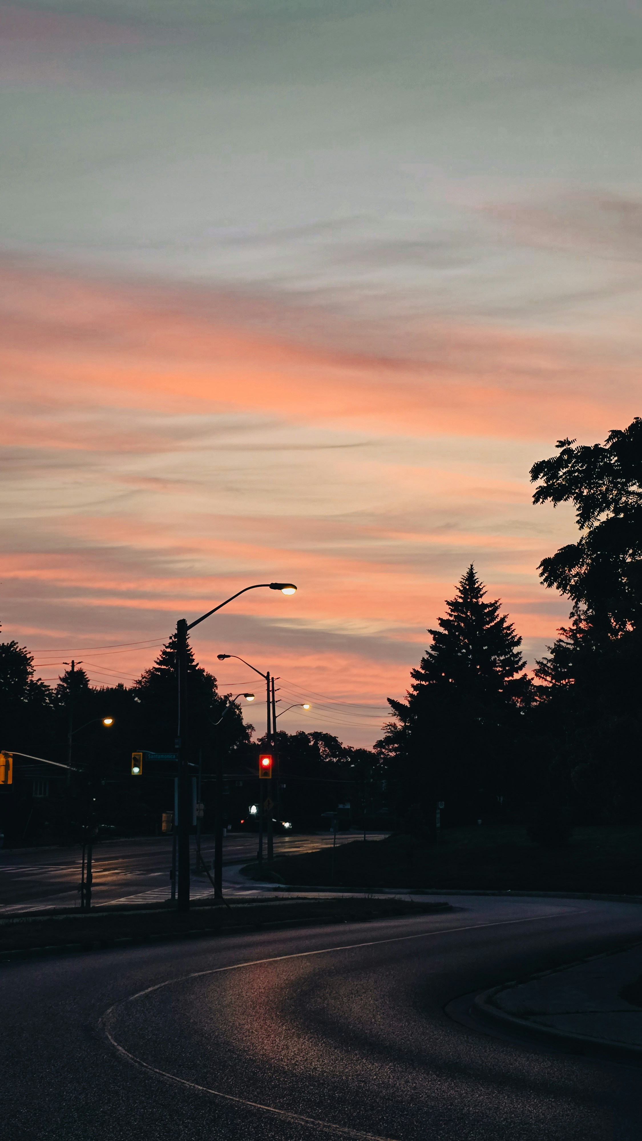 Road curves through trees at sunset with colorful sky