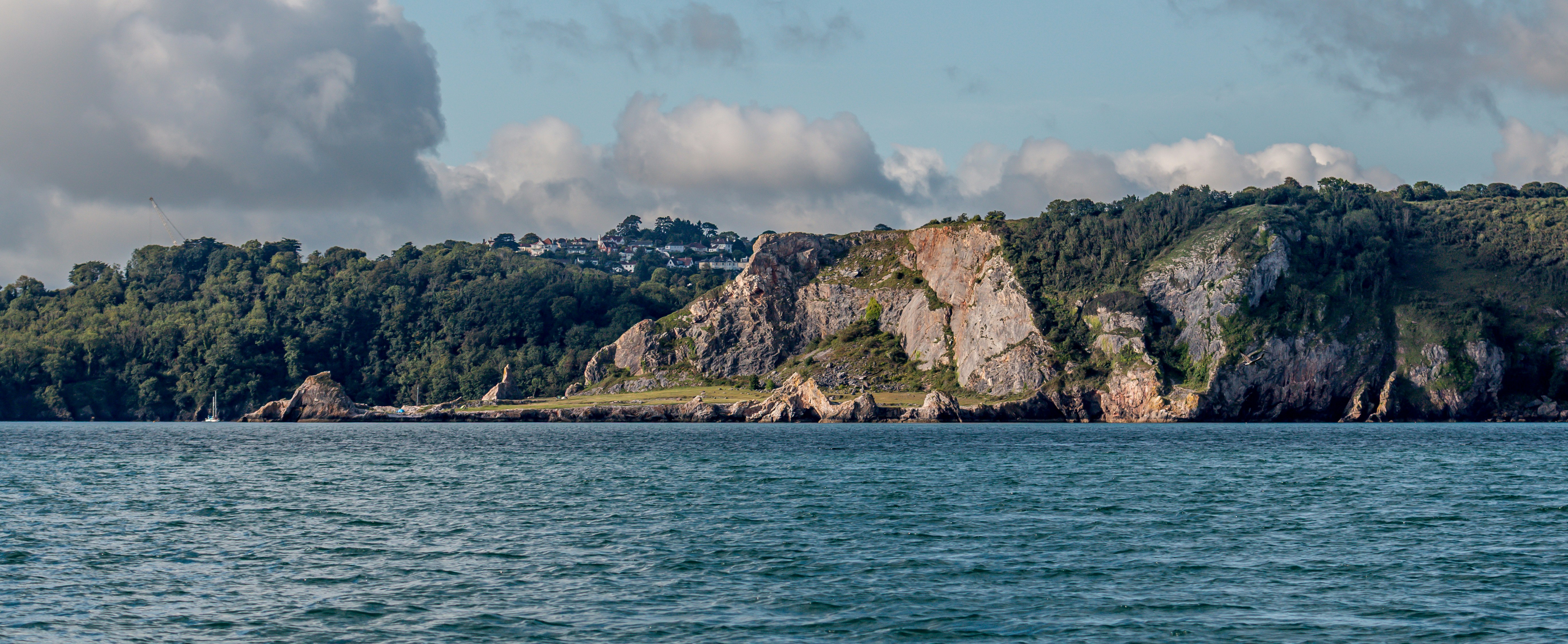Rocky cliffs covered in green trees meet the blue ocean.