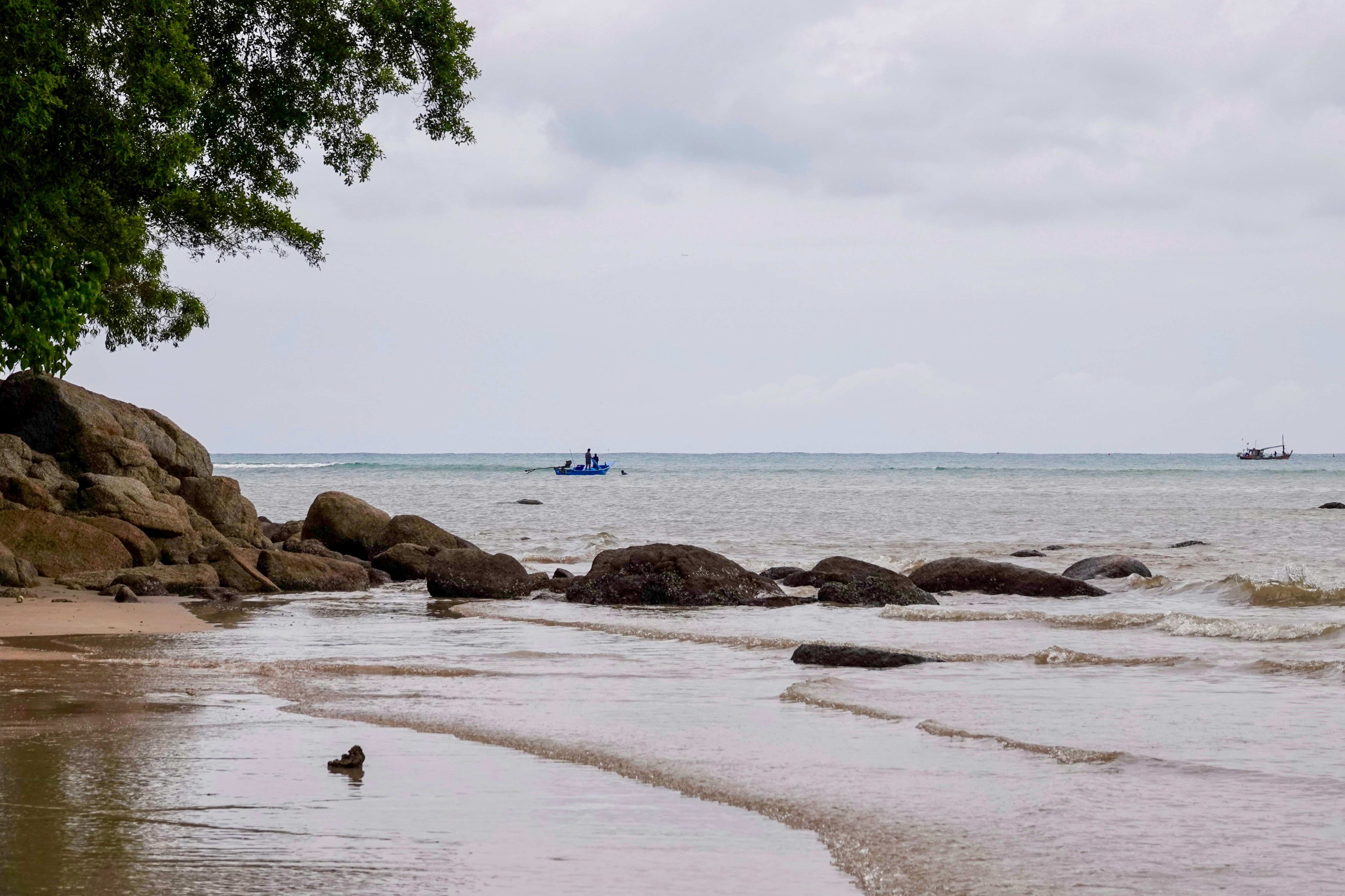 Spiaggia rocciosa con oceano calmo e barca lontana