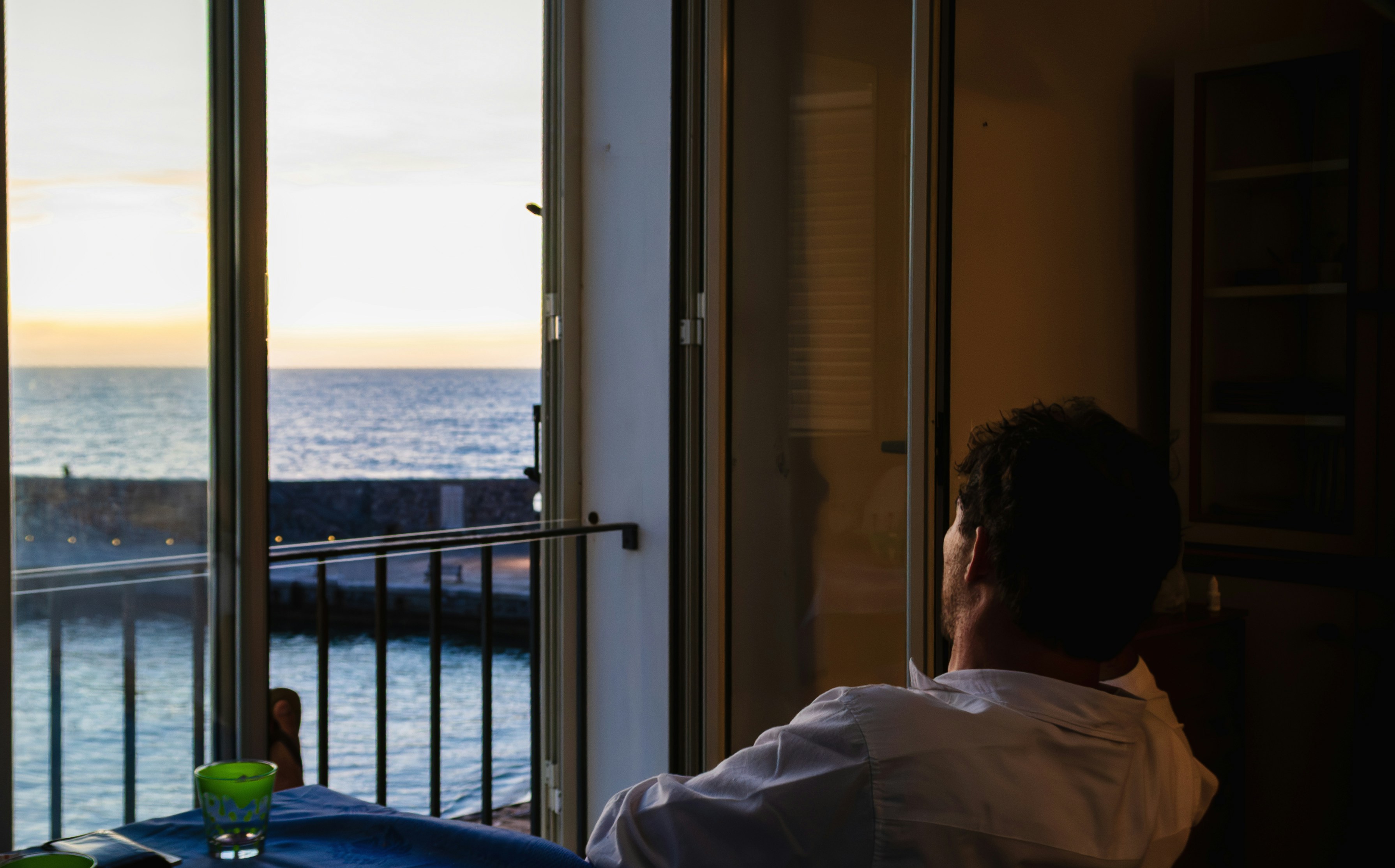 Man looking out window at the ocean sunset