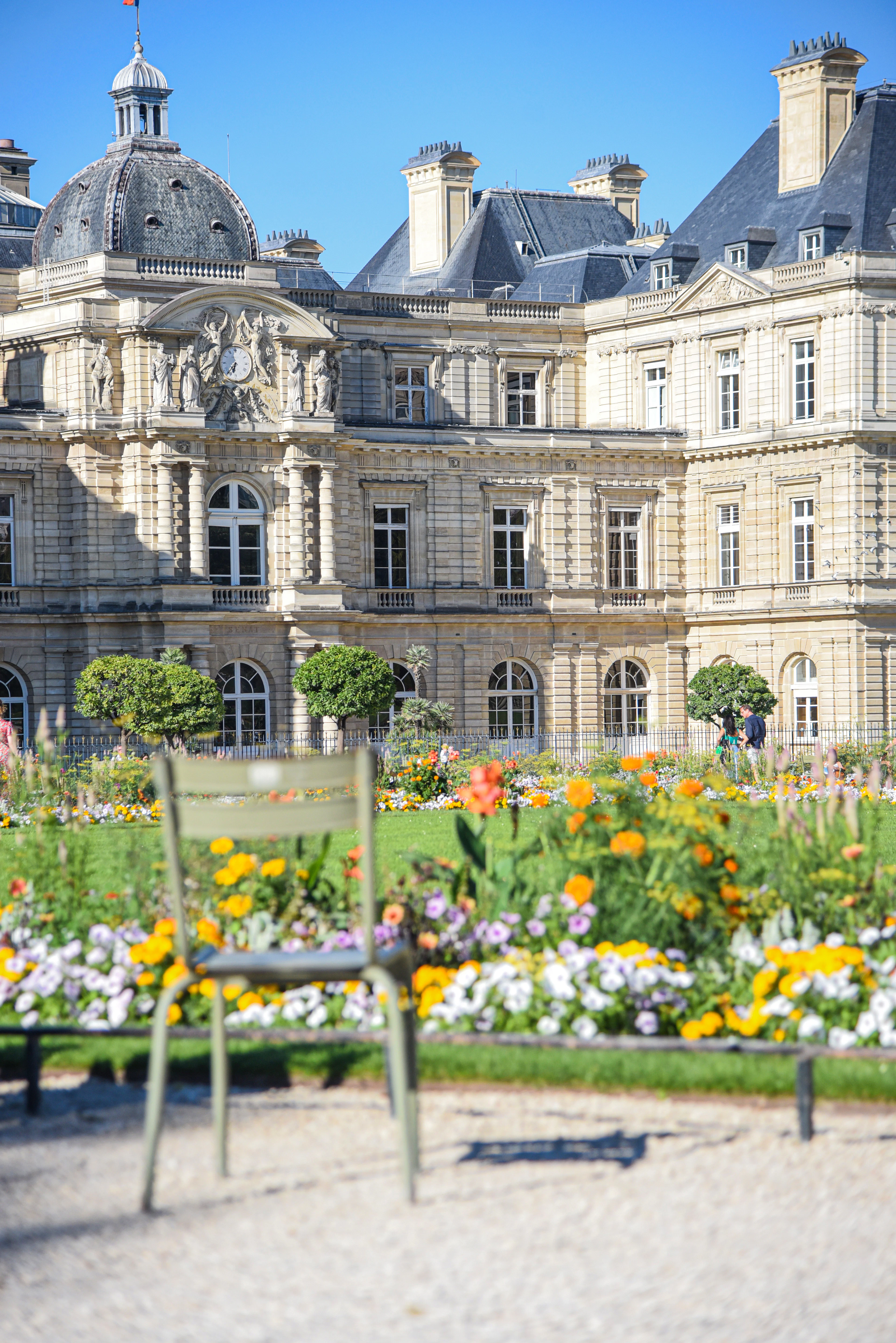 A green metal park chair in front of flowerbeds and the carved stone facade of the Luxembourg Palace, Jardin du Luxembourg, Paris