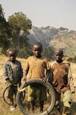 Three young boys stand with a tire outdoors.