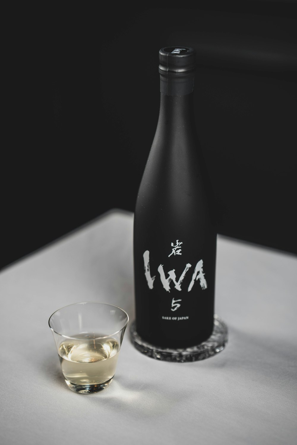 Black Junmai sake bottle with a clear tasting glass on a dark table