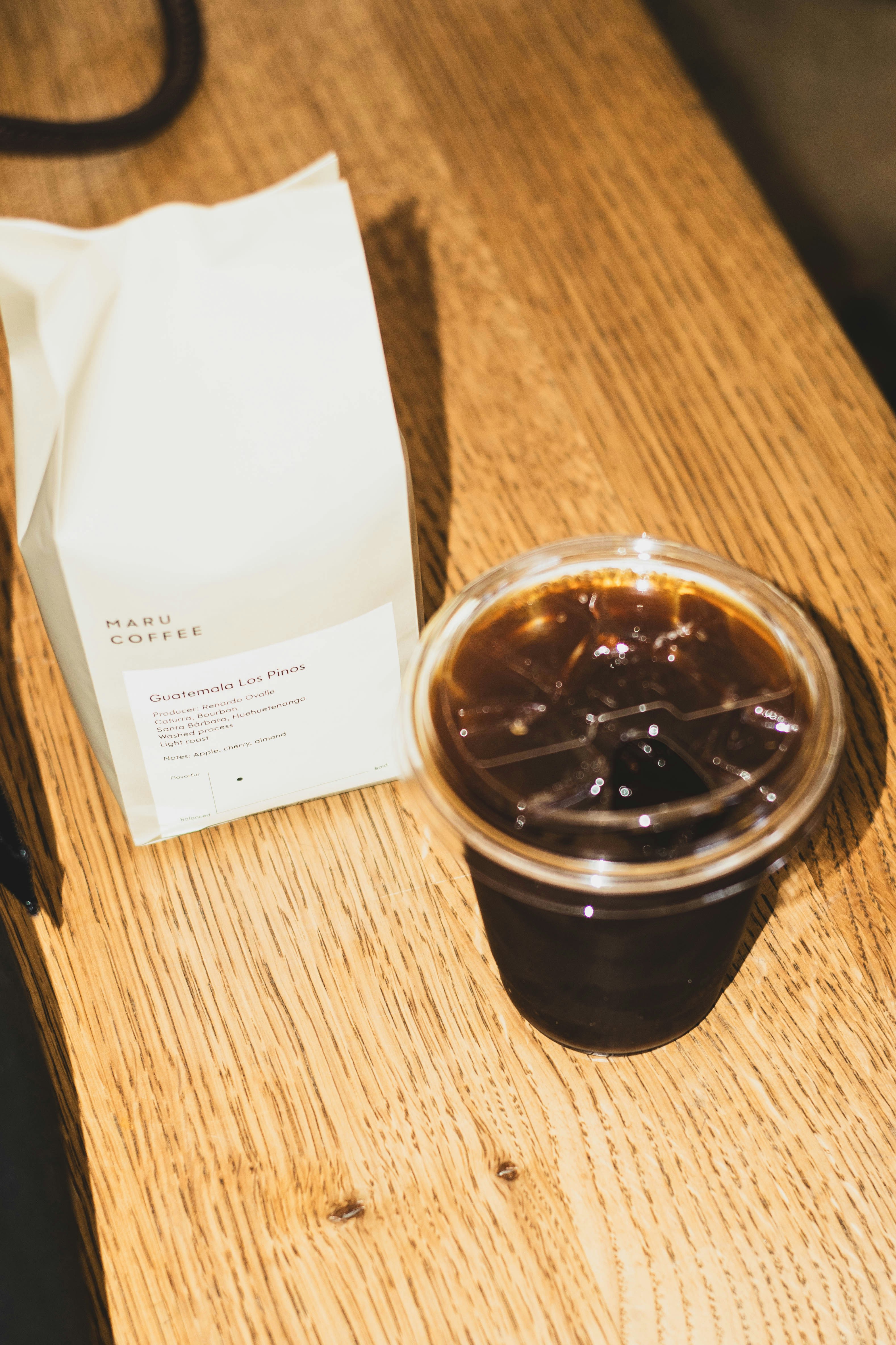 Café gelado e saco de grãos de café na mesa de madeira.