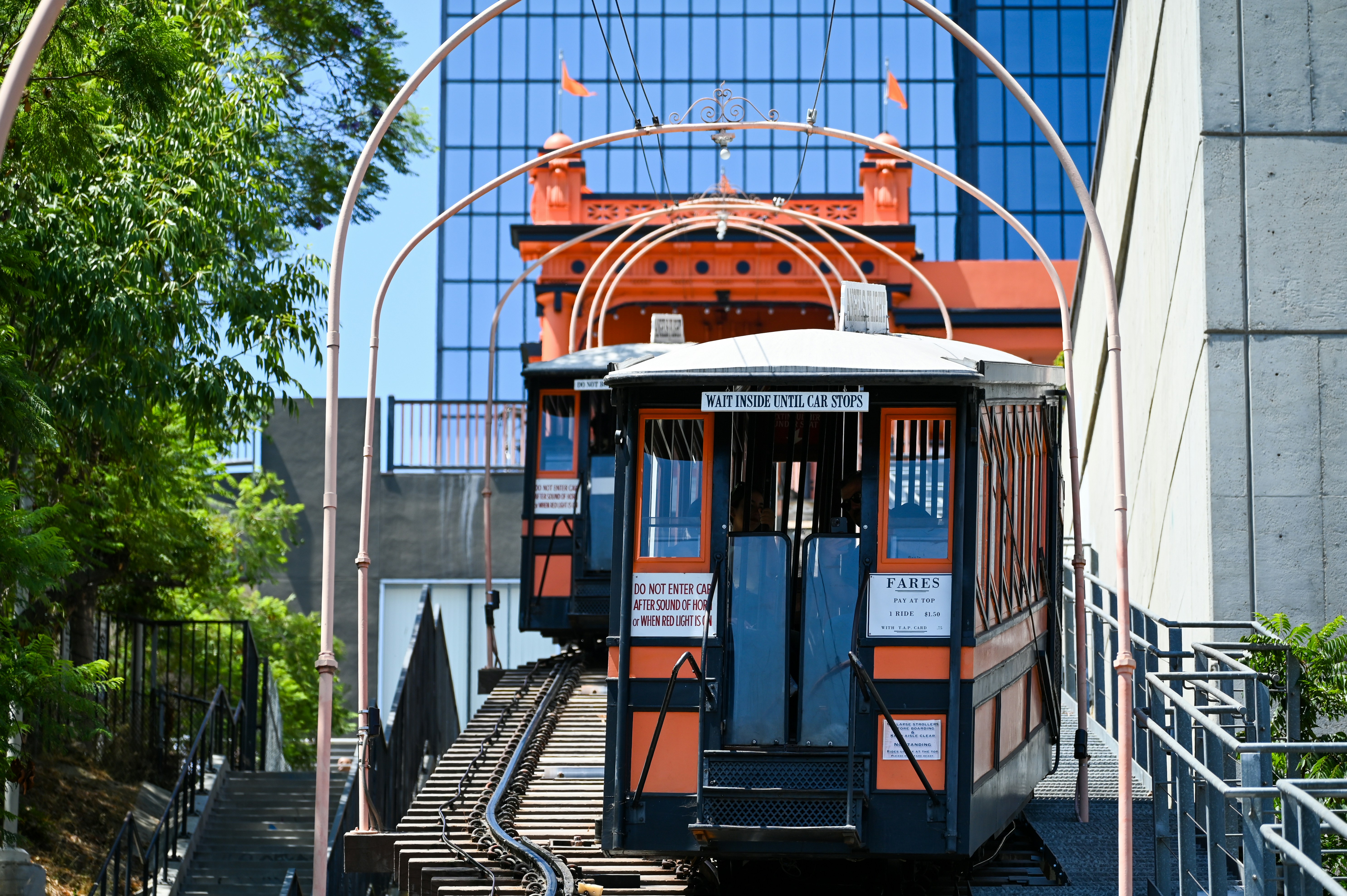 Orange and black funicular cars on tracks ascending hill.