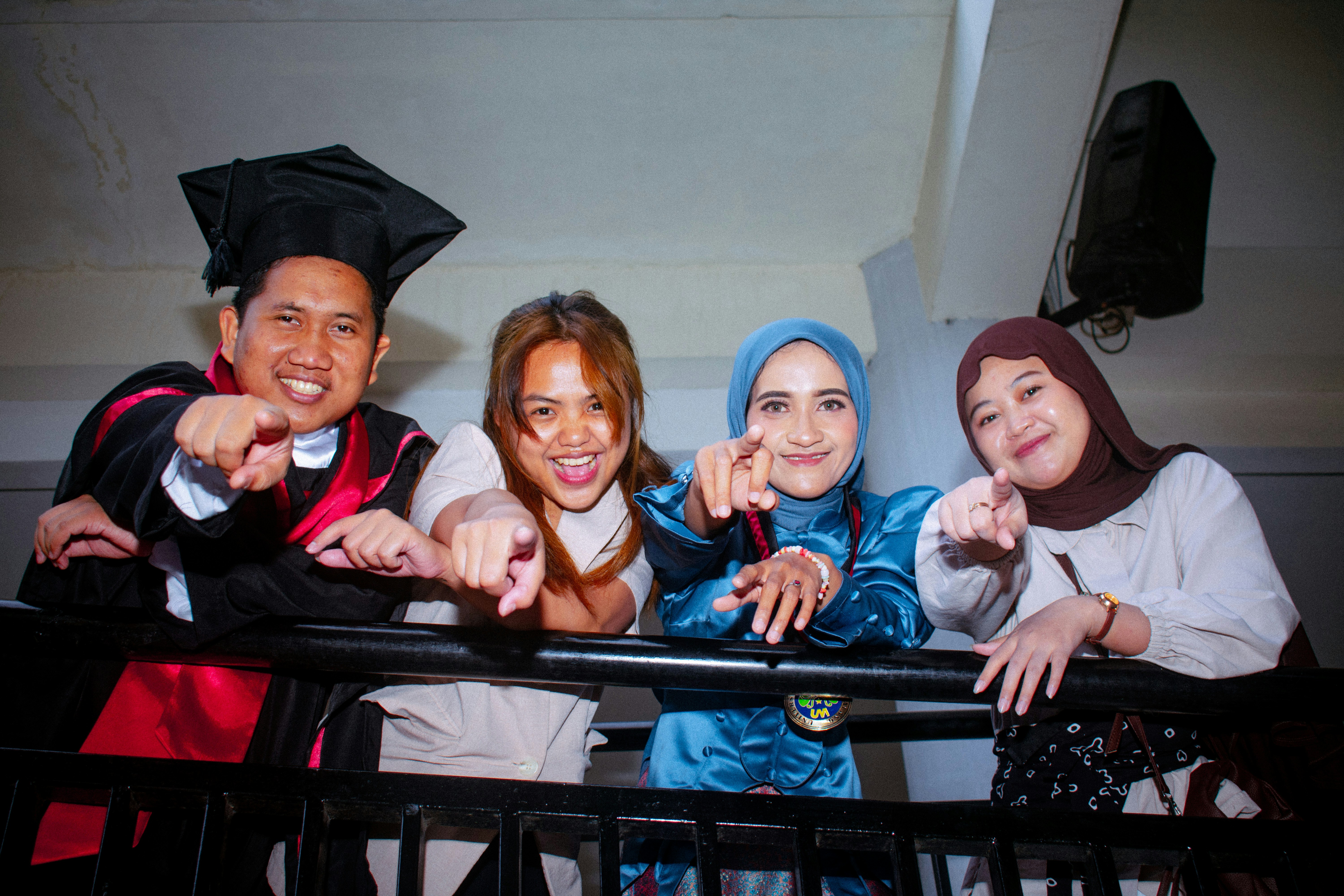 Four smiling graduates pointing forward