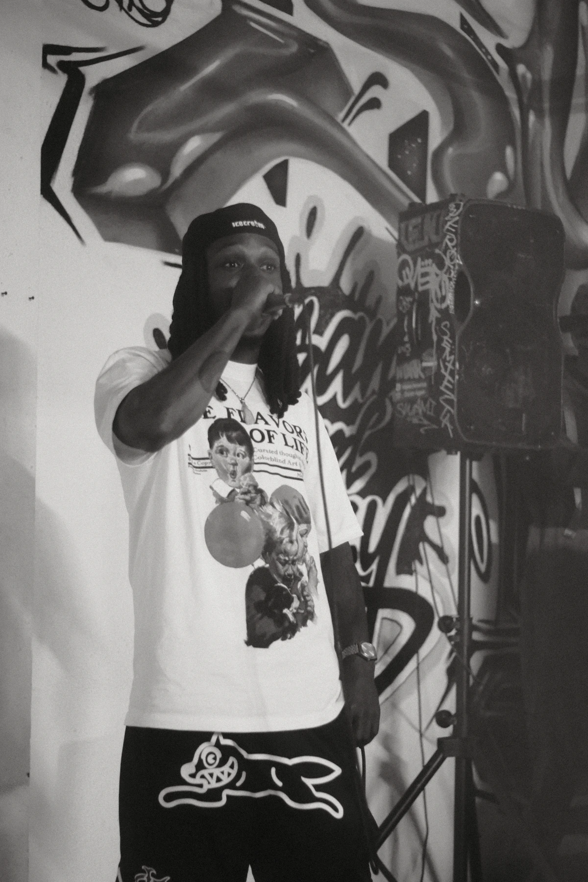 A rapper holds a microphone in front of a graffiti-covered wall