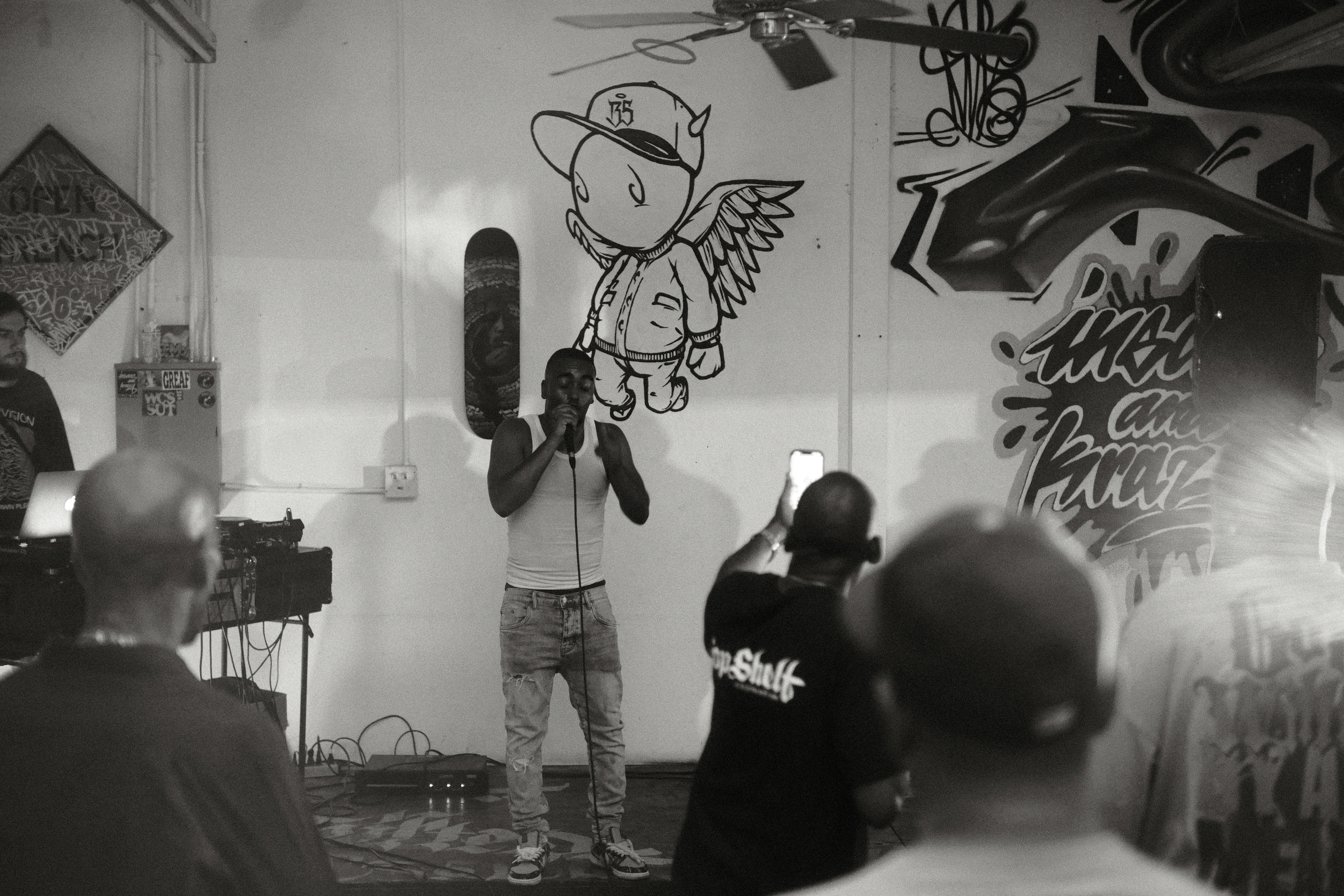 Man performs for a crowd in a graffiti-covered room.