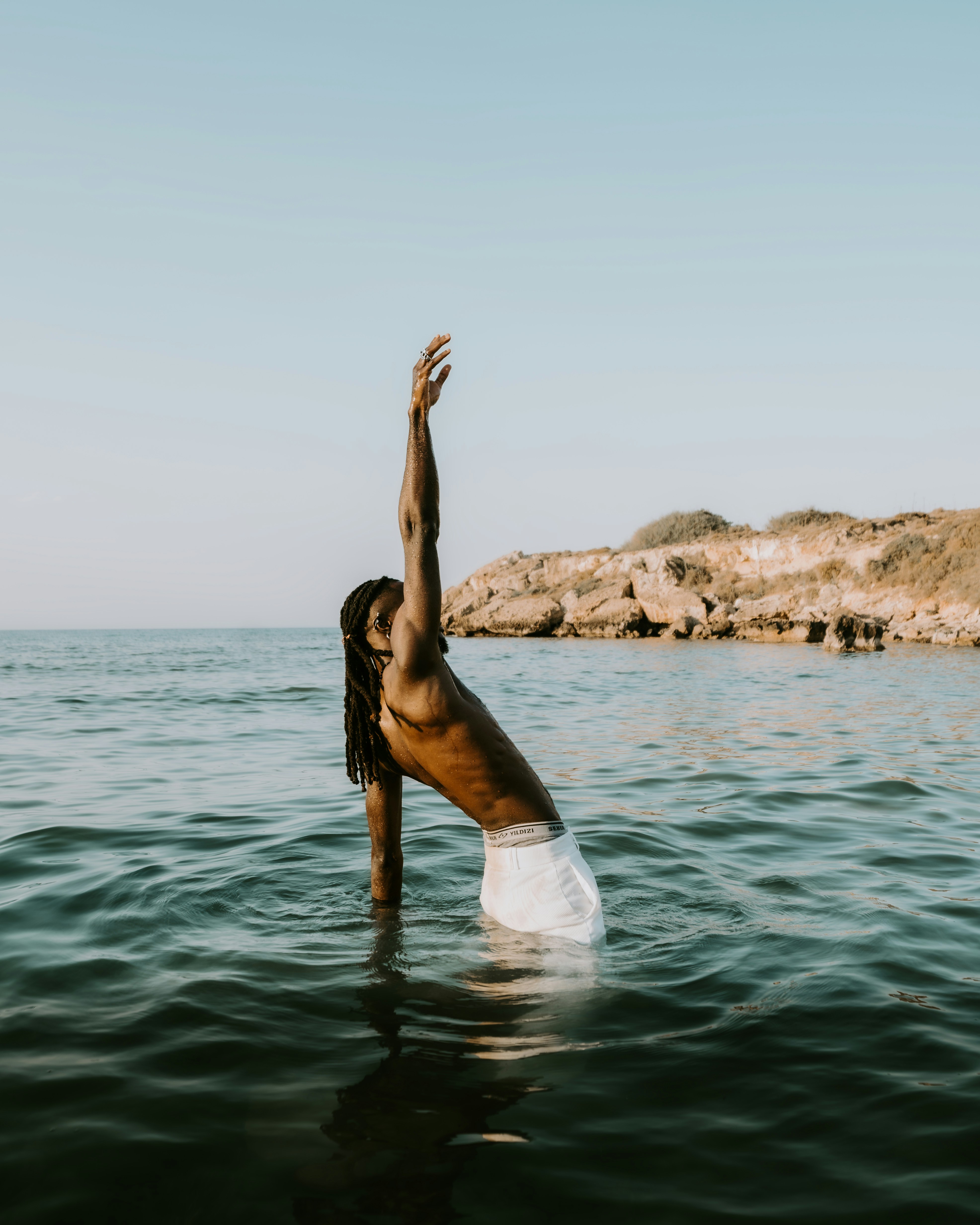 Hombre con rastas en pantalones cortos blancos en el océano.
