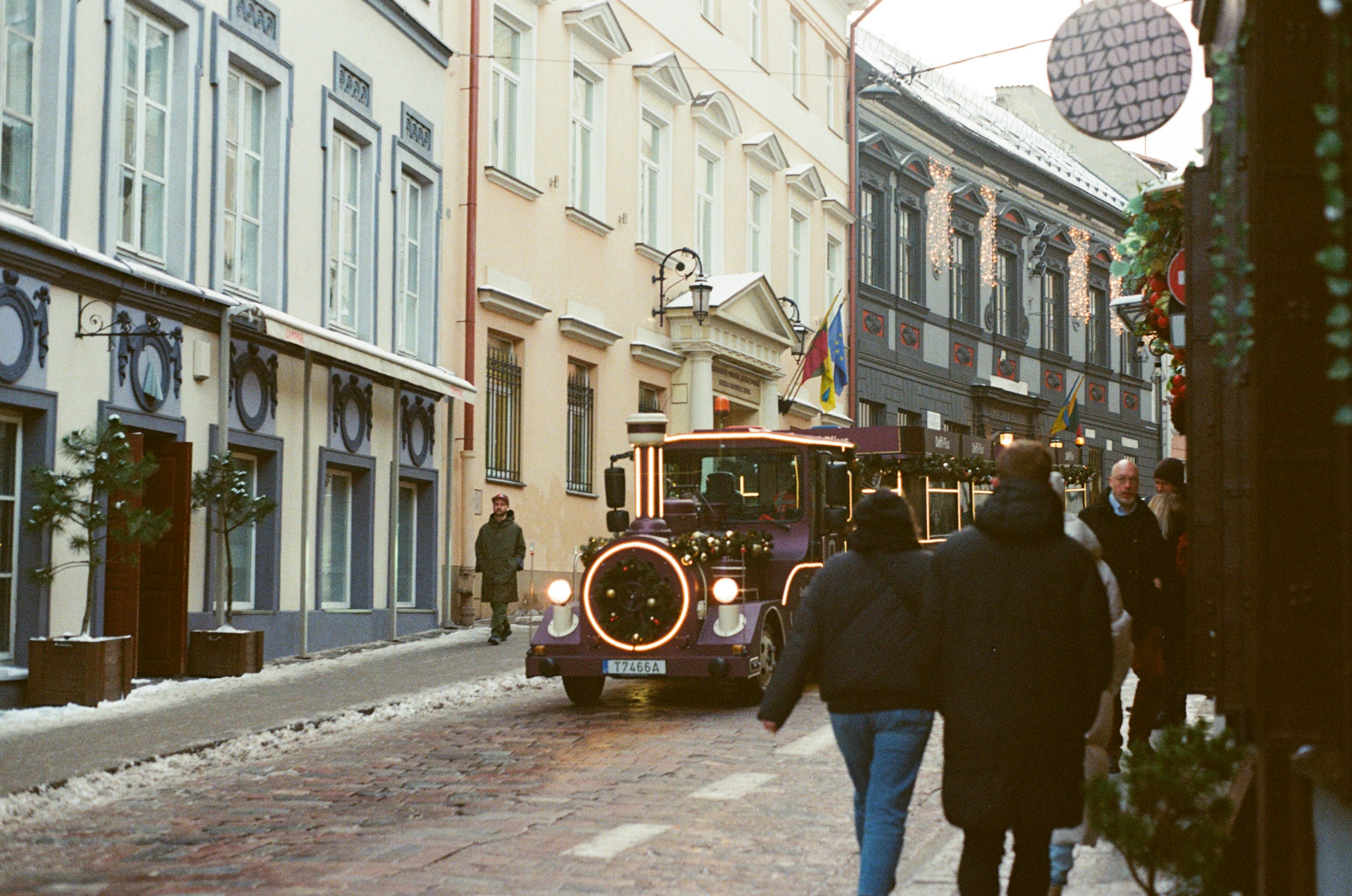 A festive train travels down a snowy street.