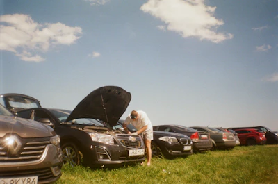 Man working on car engine outdoors with parked cars
